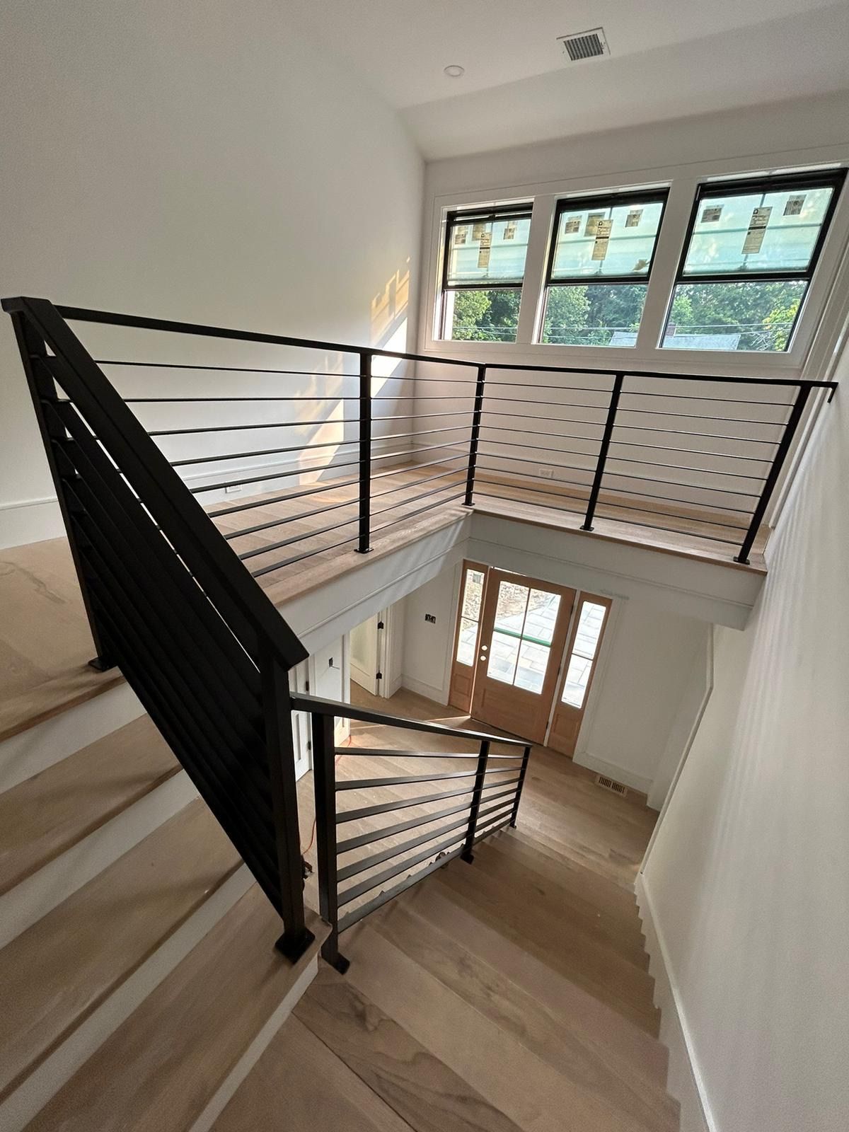 Modern stairwell with black railings, light wood steps, and windows above a front door