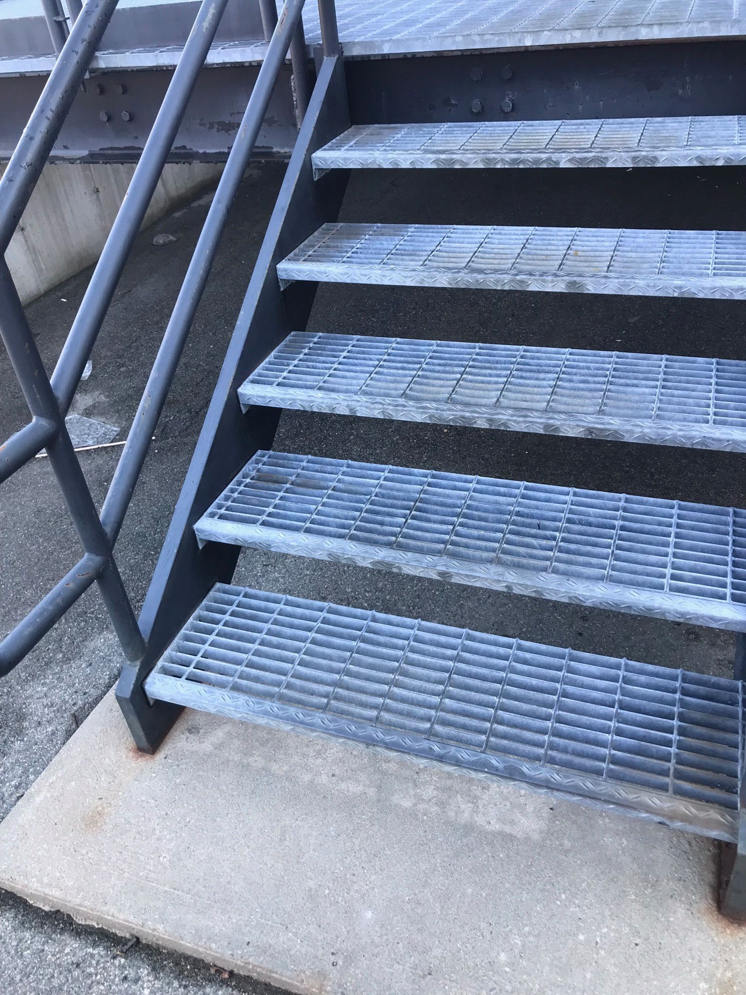 Metal outdoor staircase with gray steps and black railings, seen from the bottom.
