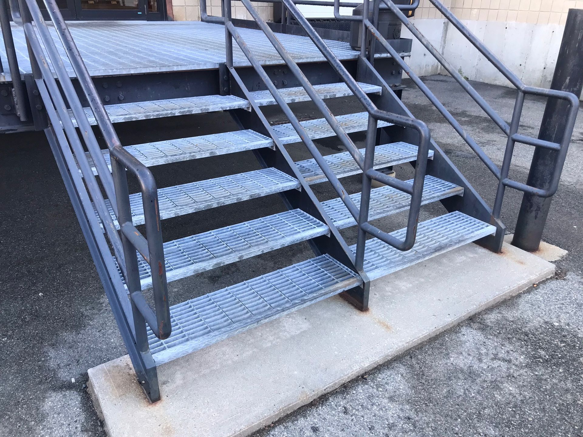 Metal outdoor stairs with black handrails and a concrete landing beside a building