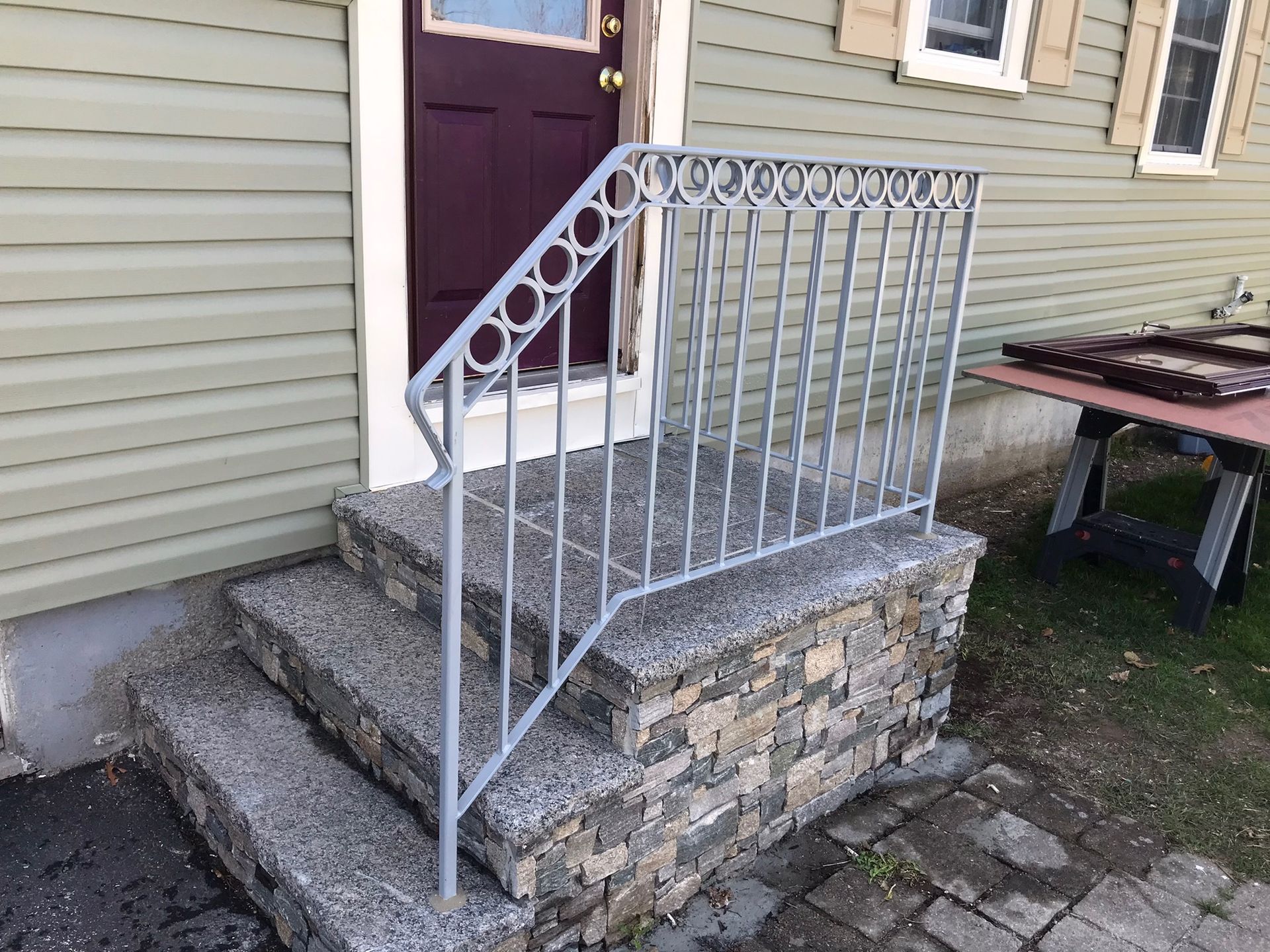 White metal handrail beside stone steps leading to a house door and porch.