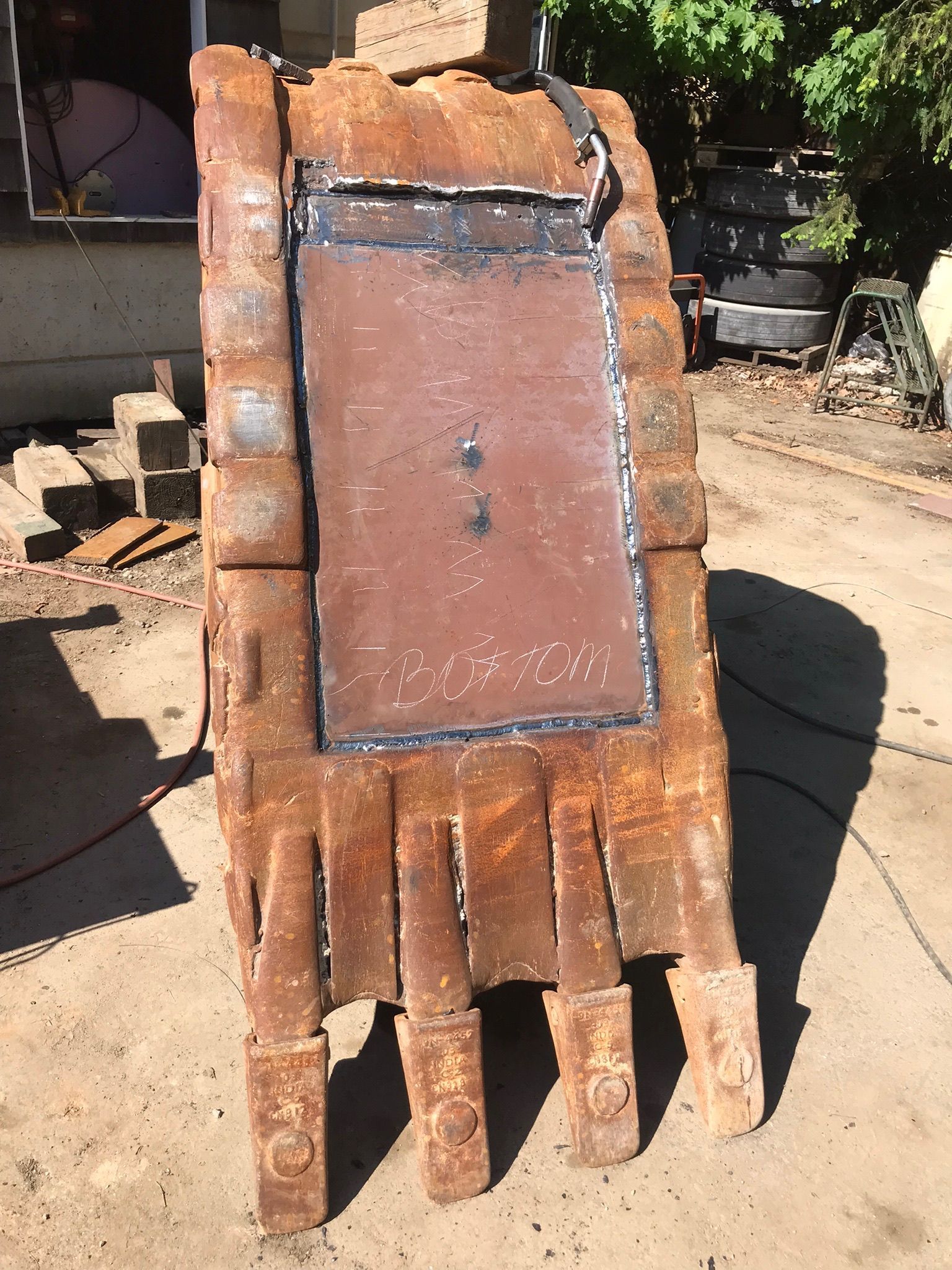 Rusty metal hand-shaped sculpture with five fingers, standing outdoors in a yard