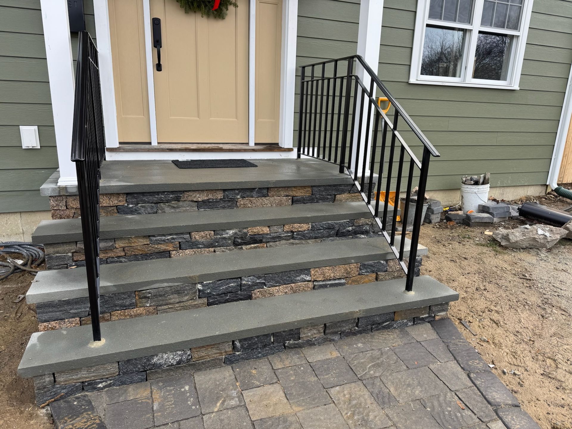 Front steps to a house with black railings, worn stone treads, and a tan front door.