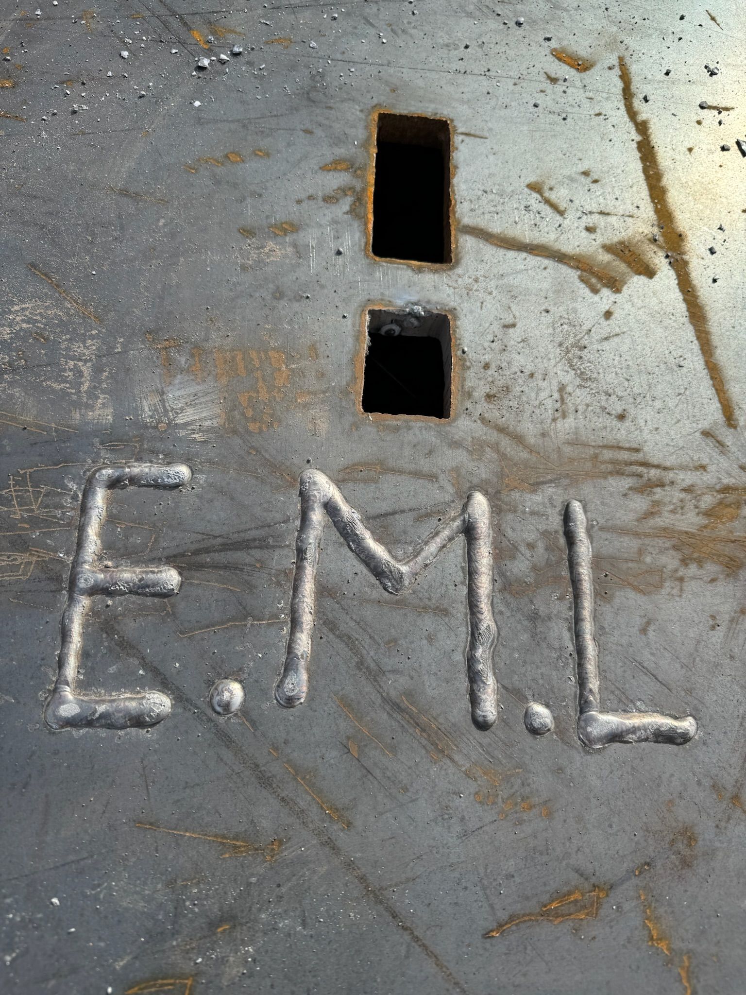 Concrete floor with two rectangular openings and the letters “EML” scratched below them.