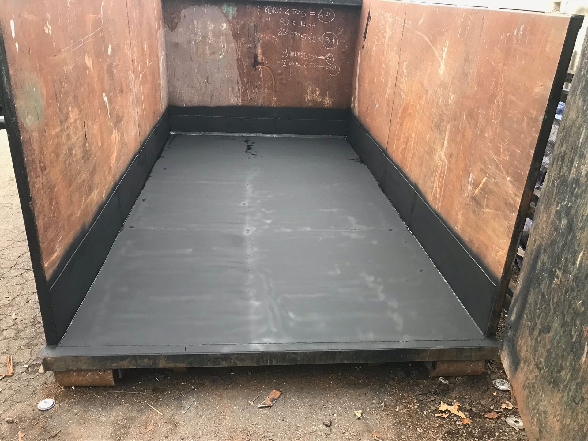 Empty dumpster with a freshly lined black floor and rust-colored metal walls.