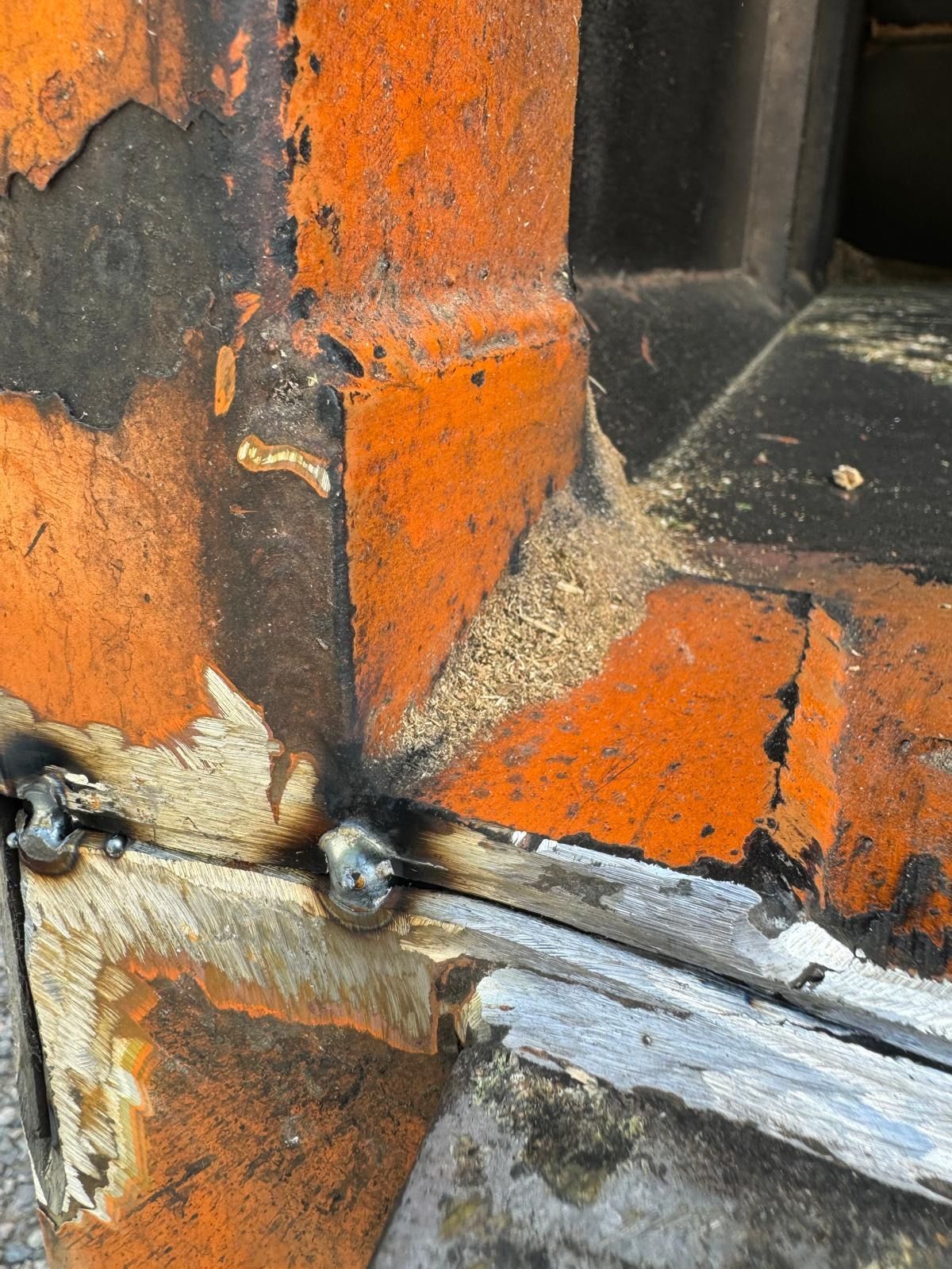 Close-up of a rusted metal seam with orange paint peeling and a black bolt on the edge