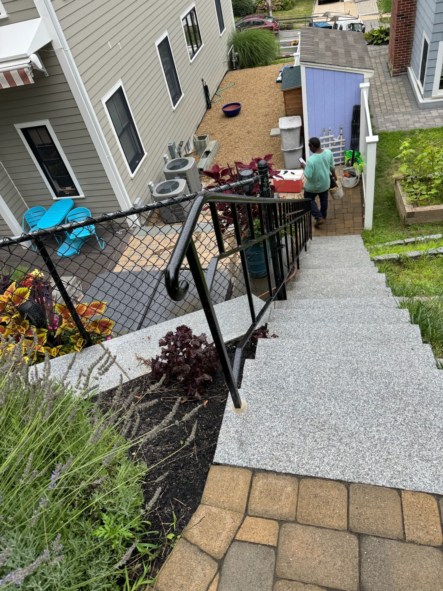 Backyard gravel path beside a house, with a person standing near a patio and garden beds.