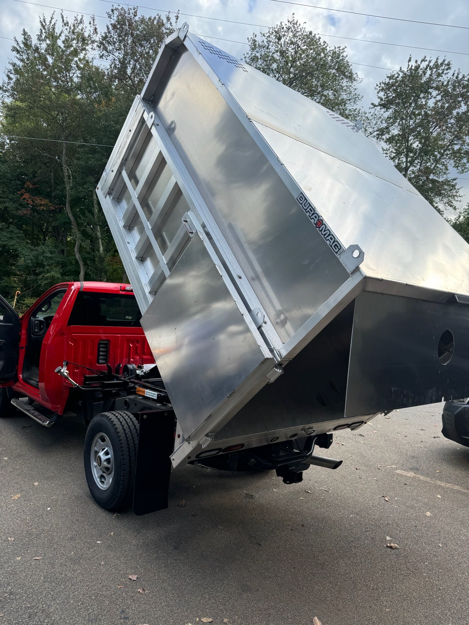 Red dump truck with raised silver bed on a paved road outdoors