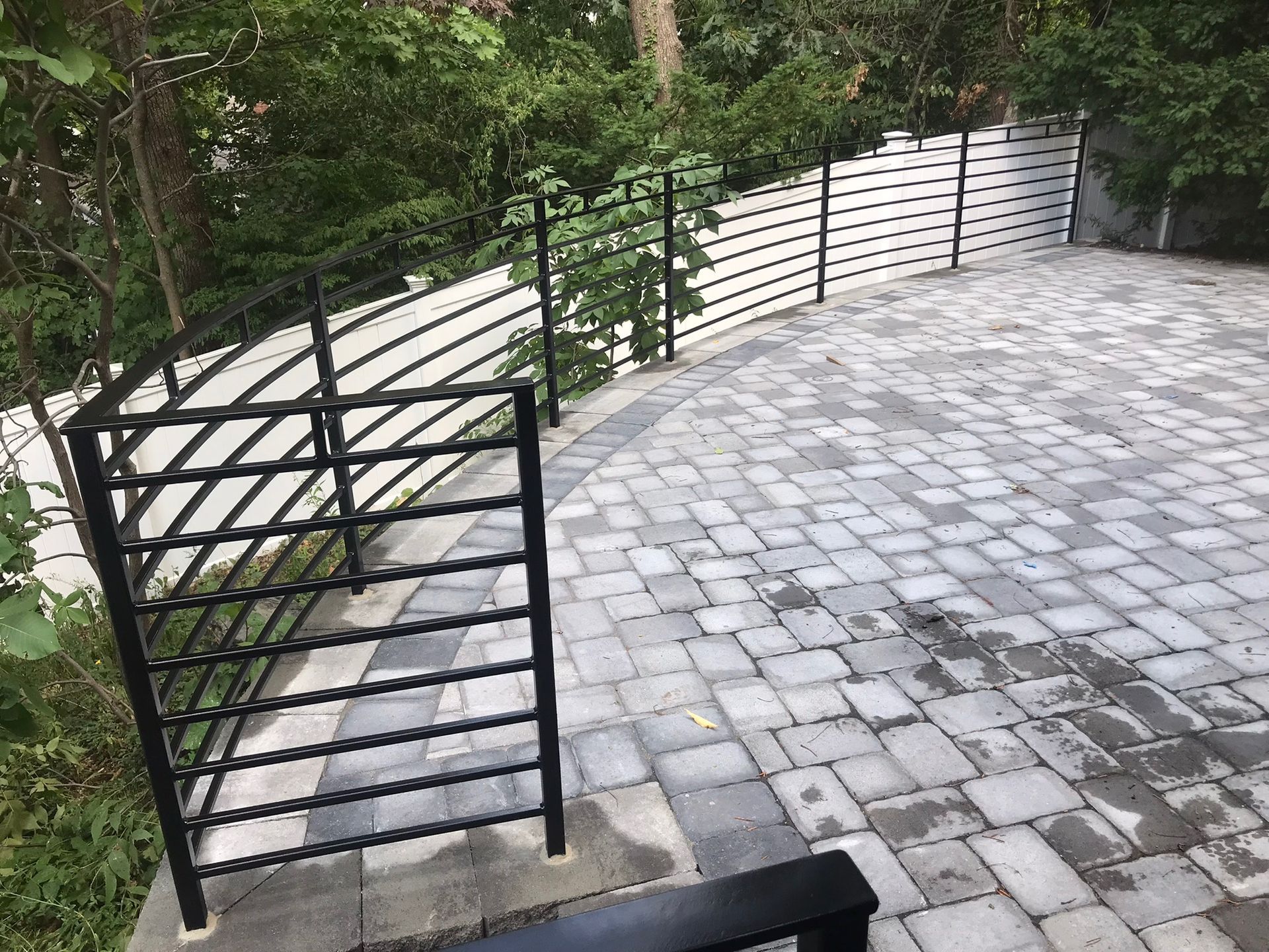 Curved stone patio with black metal railings and stairs beside a wooded hillside