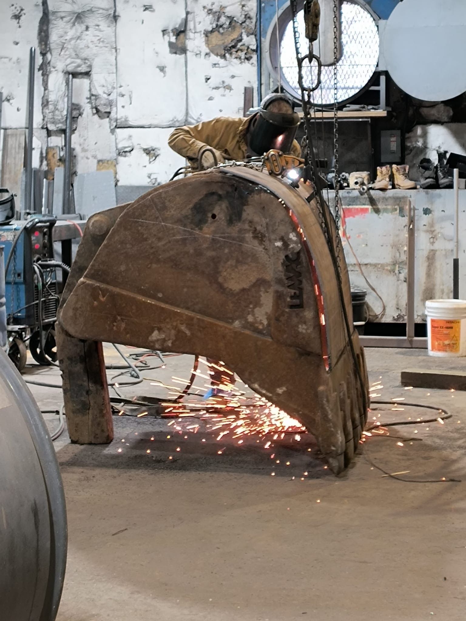 Worker cutting a large rusted metal shell with sparks flying in a workshop