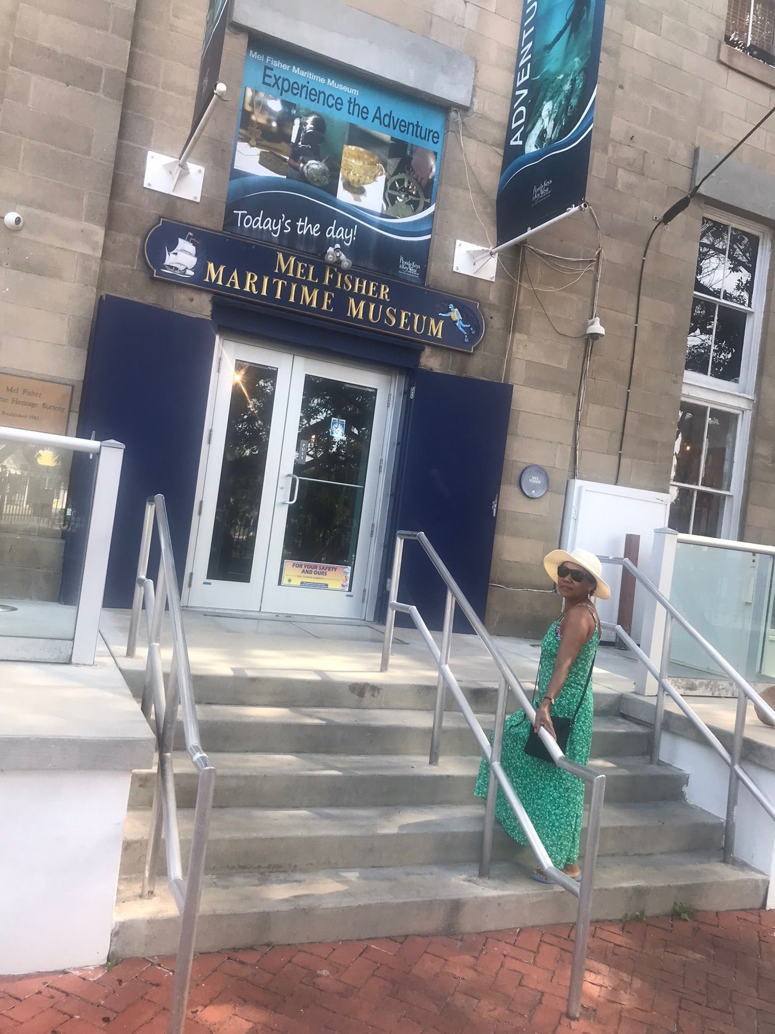 Woman in green dress sitting on steps outside a building entrance with metal handrails.