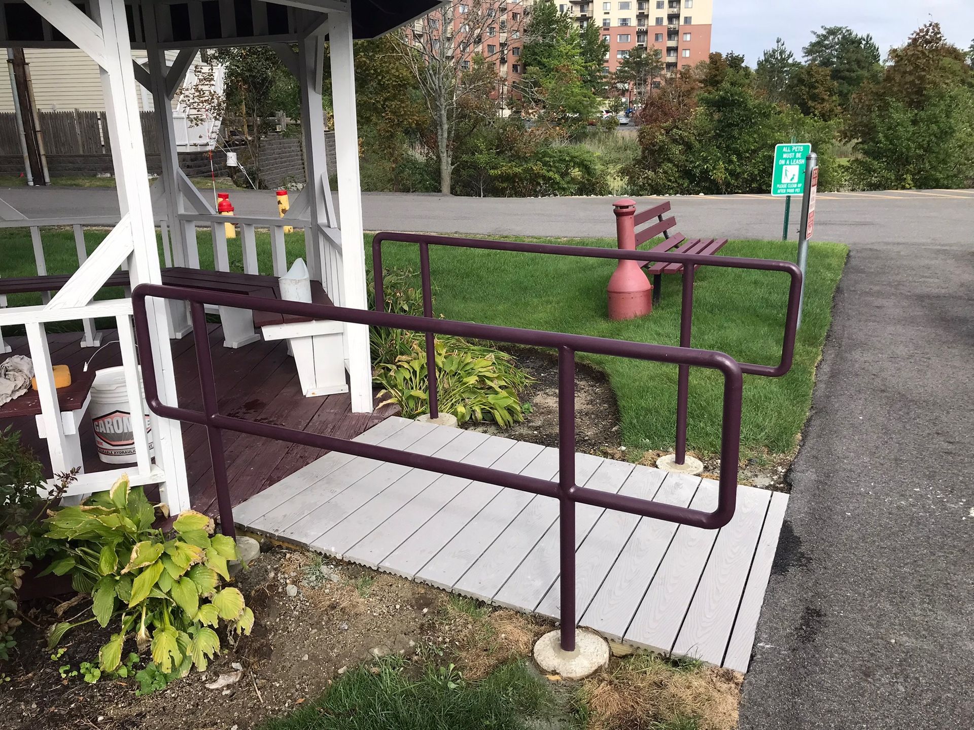Accessibility ramp with maroon handrails beside a white gazebo and a paved path outdoors