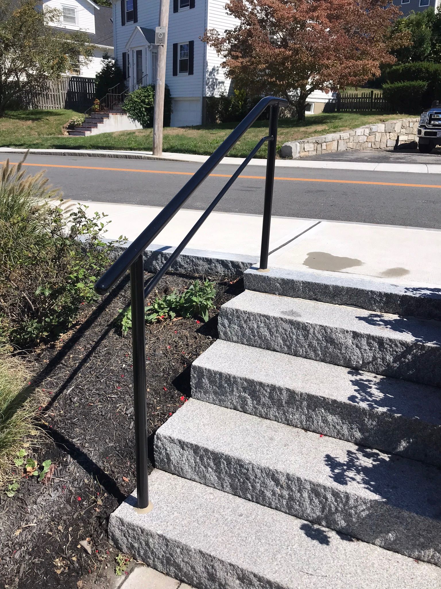 Outdoor stone steps with black handrails leading up from a sidewalk in a residential area