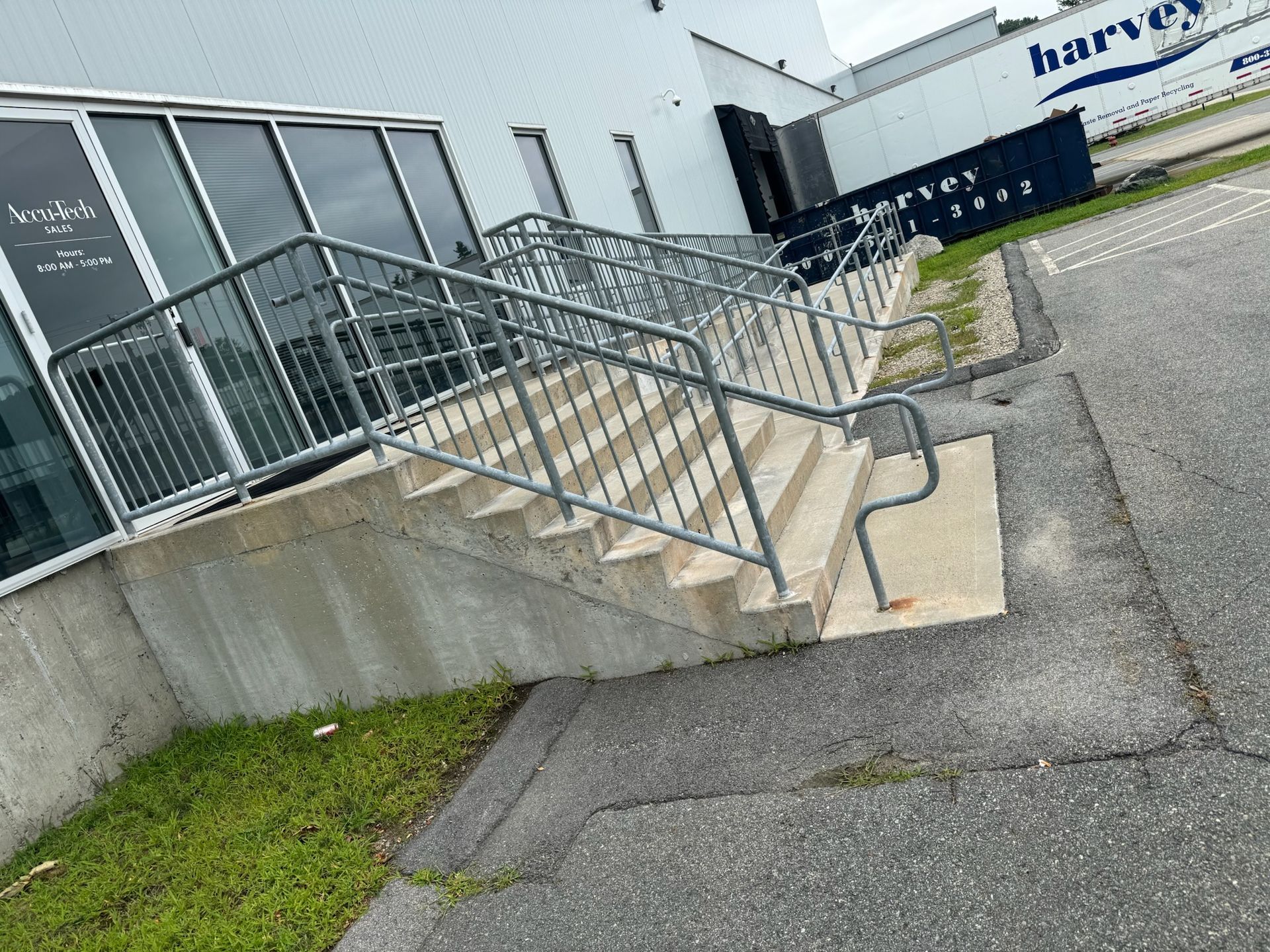 Concrete steps with metal handrails leading to a building entrance beside a sidewalk and grass strip
