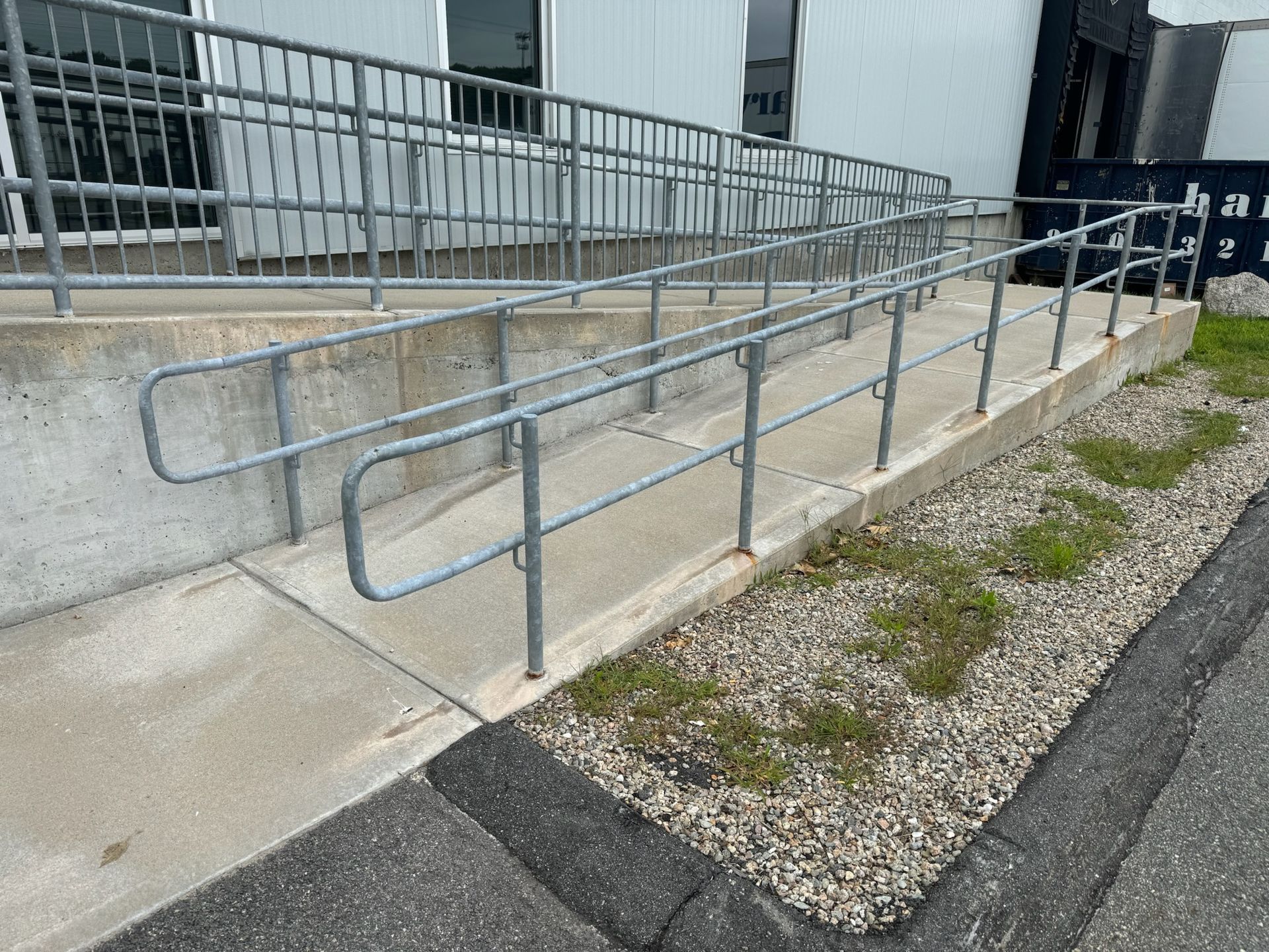 Concrete ramp with blue handrails beside a building and gravel path