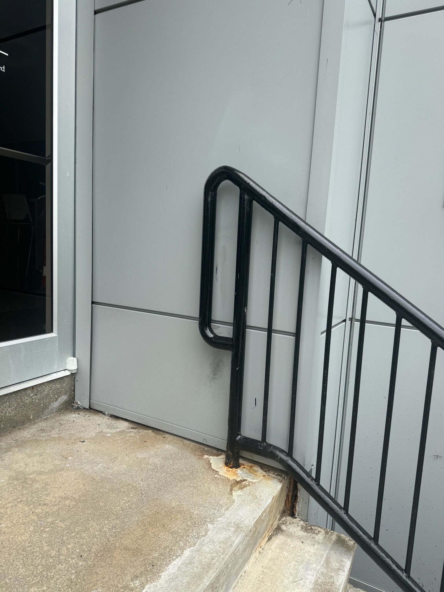 Black metal handrail beside a gray building wall and concrete step by a doorway
