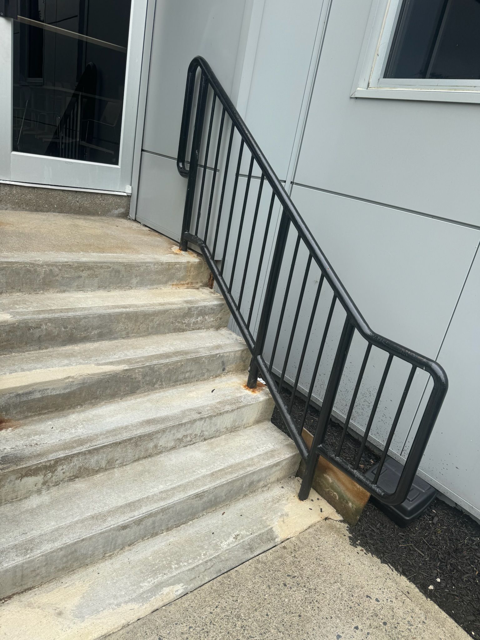 Concrete steps with a black metal handrail beside a building entrance