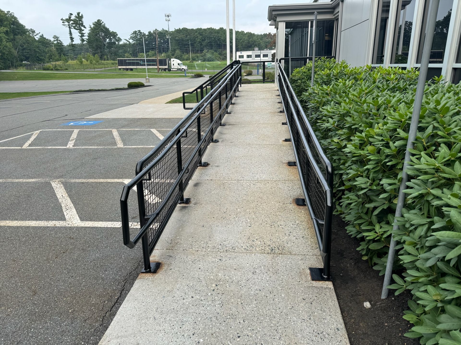 Accessible walkway with black handrails beside a parking lot and building entrance