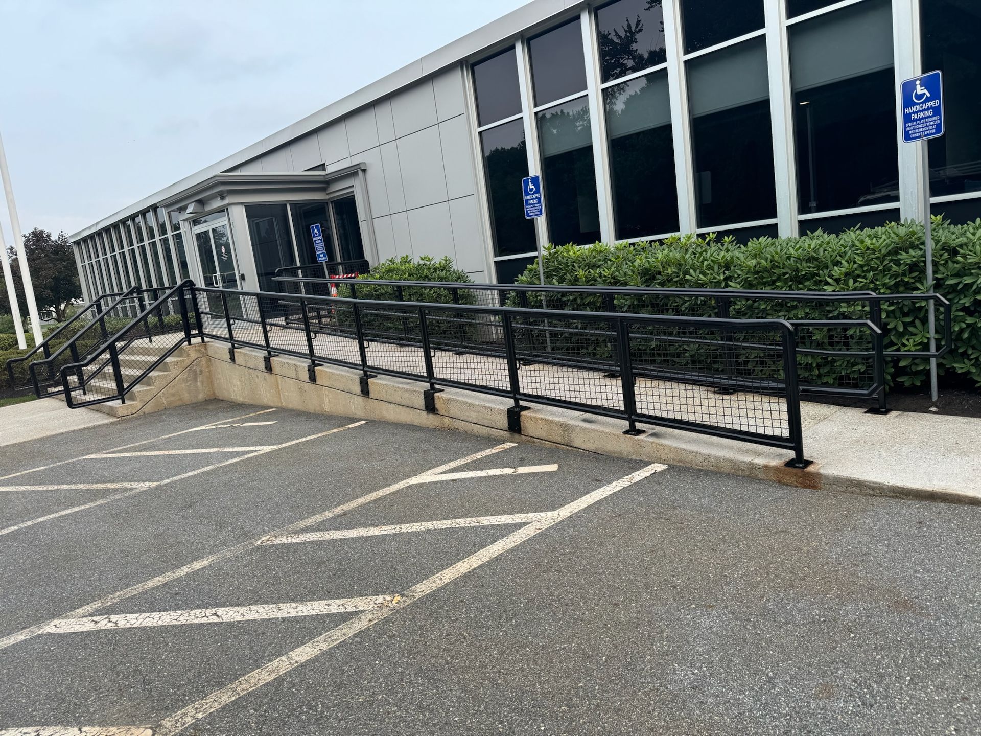 Accessible parking spaces and a wheelchair ramp beside a building with windows and black railings