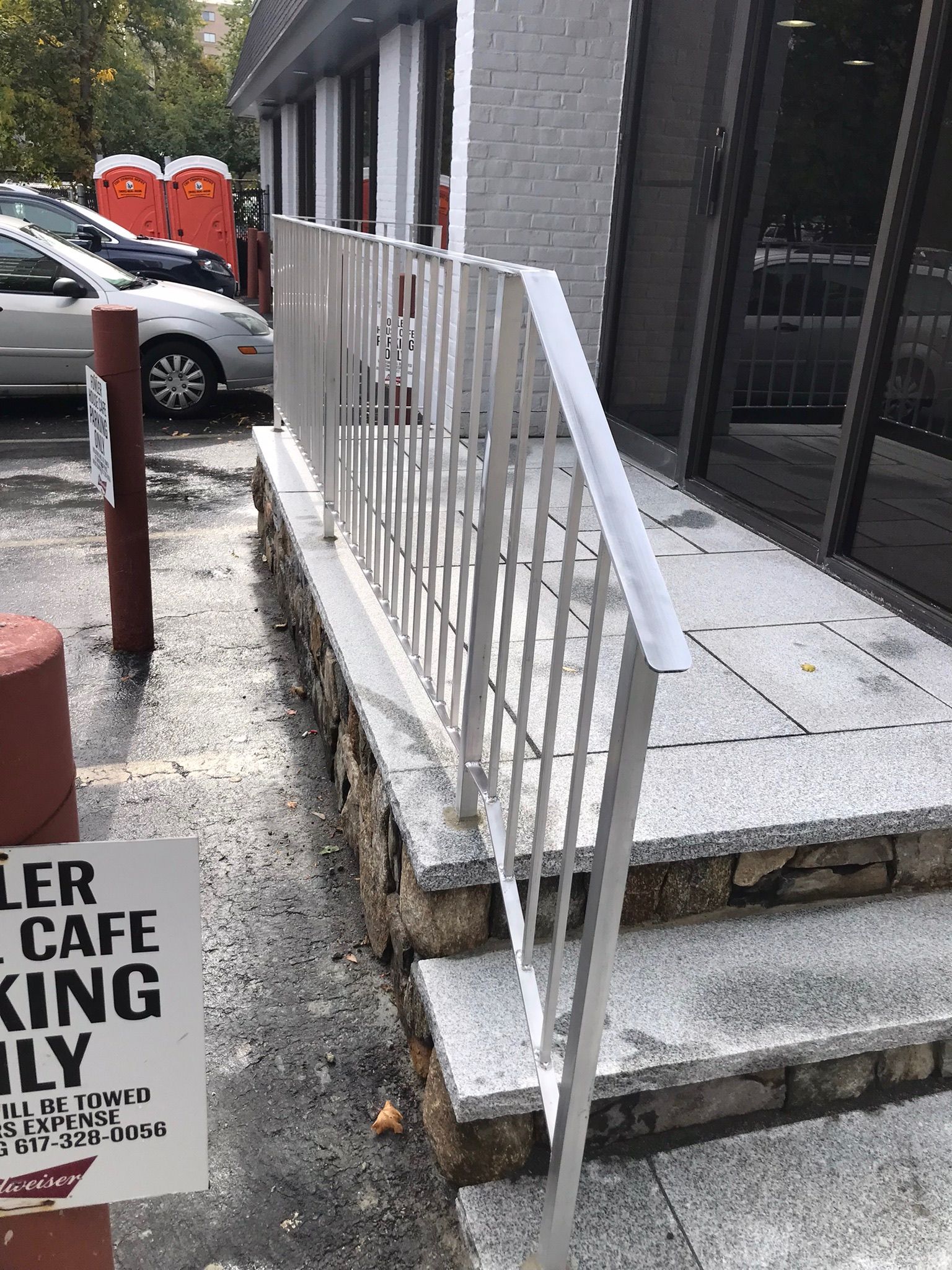 White metal ramp railing beside concrete steps and a storefront entrance on a sidewalk