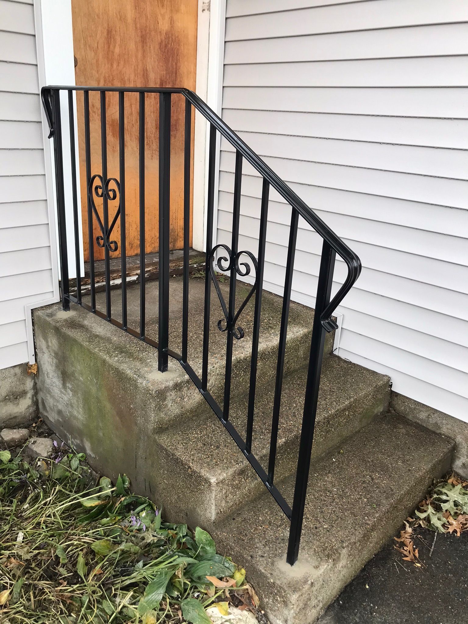Black metal railing beside concrete steps and landing at a house entrance