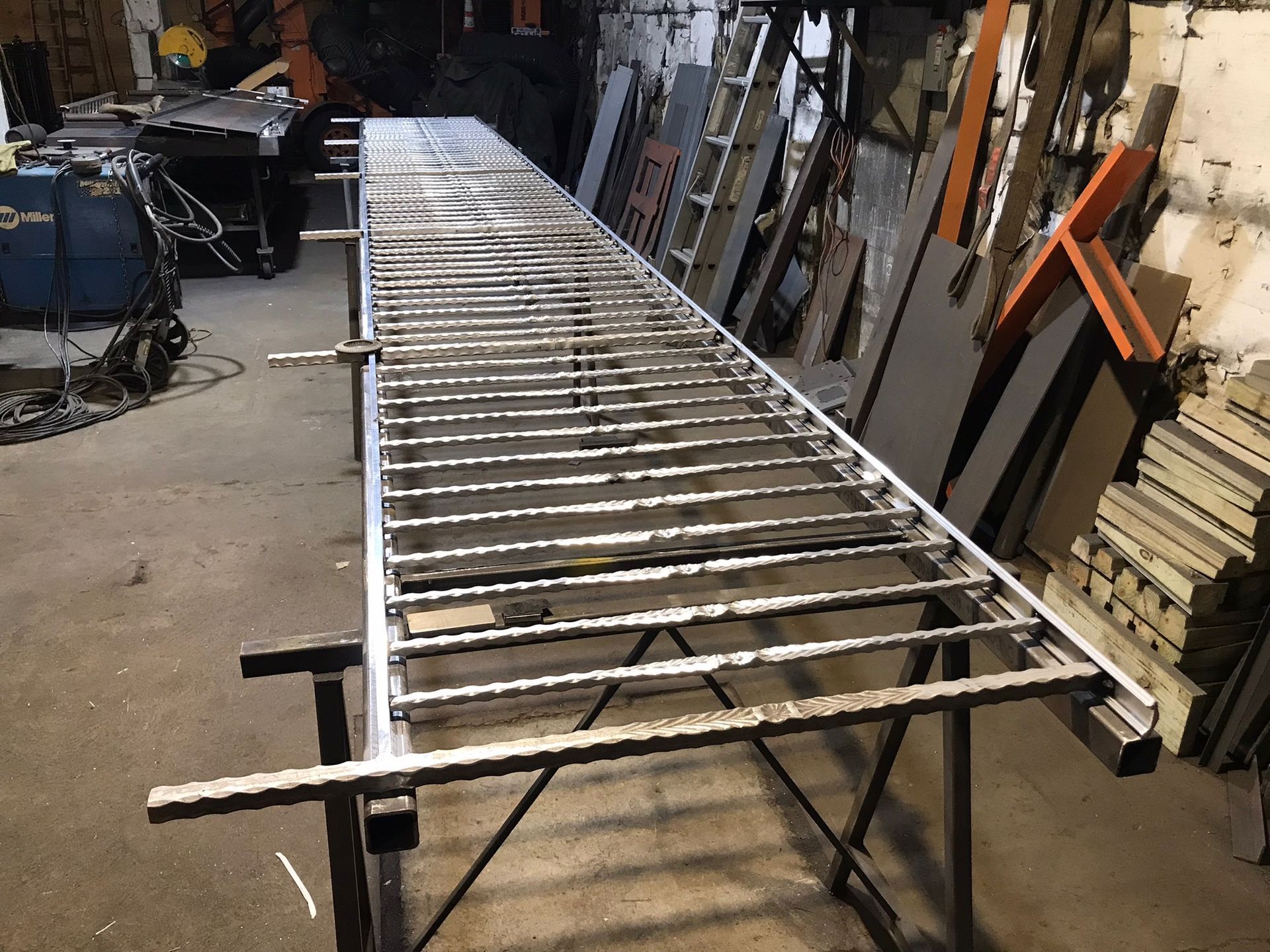 Metal ladder frame laid across sawhorses in a workshop with tools and materials in the background
