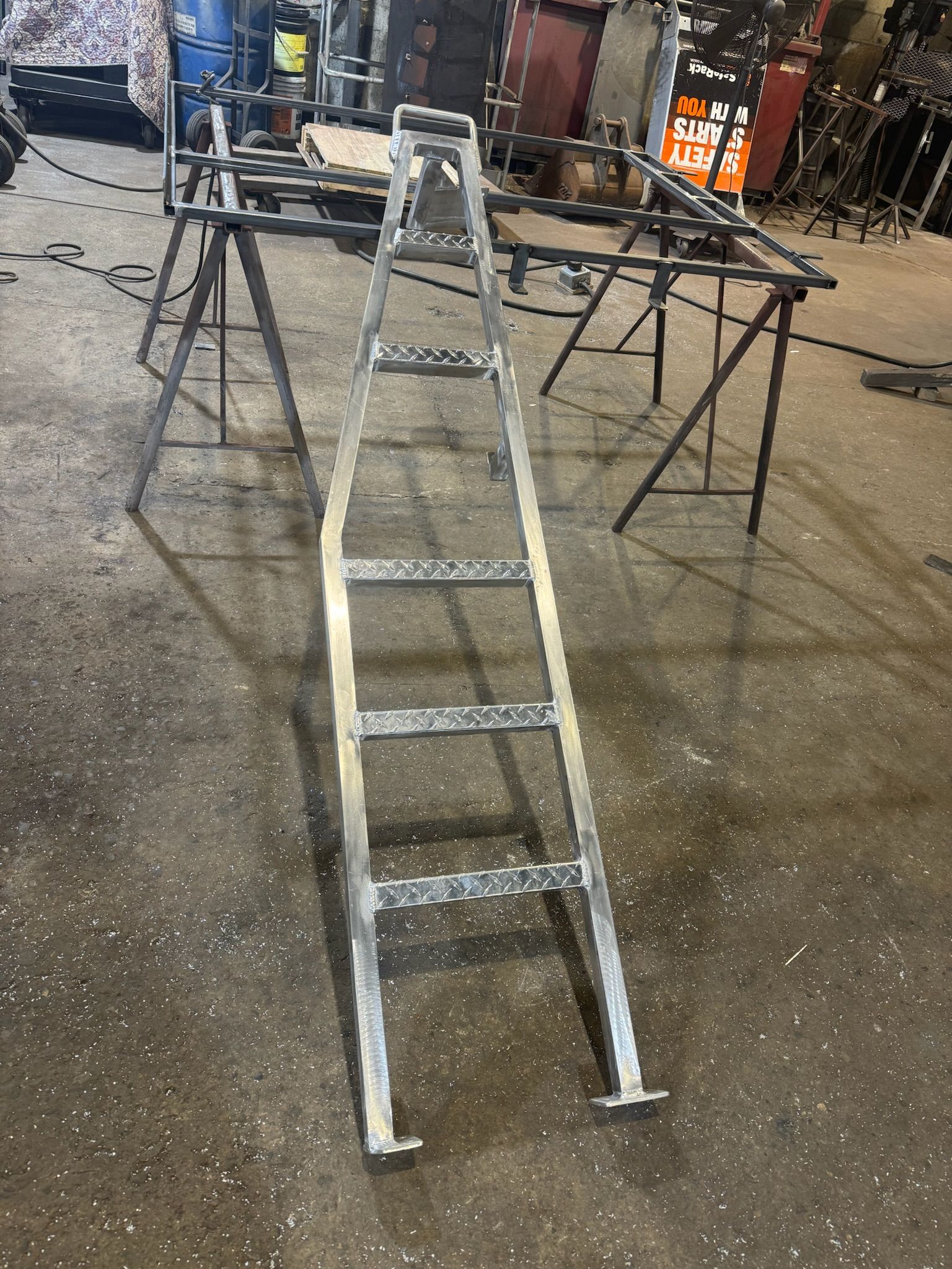 Metal step ladder in a workshop, with two sawhorses and tools in the background.