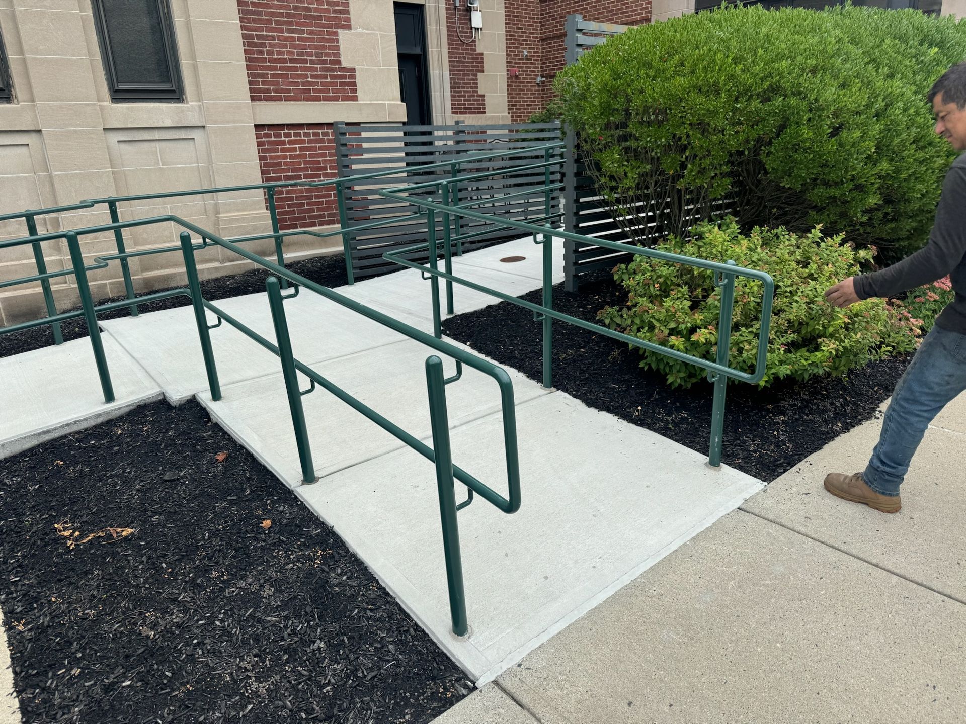 Accessible ramp with green handrails beside a building entrance; person walking nearby.