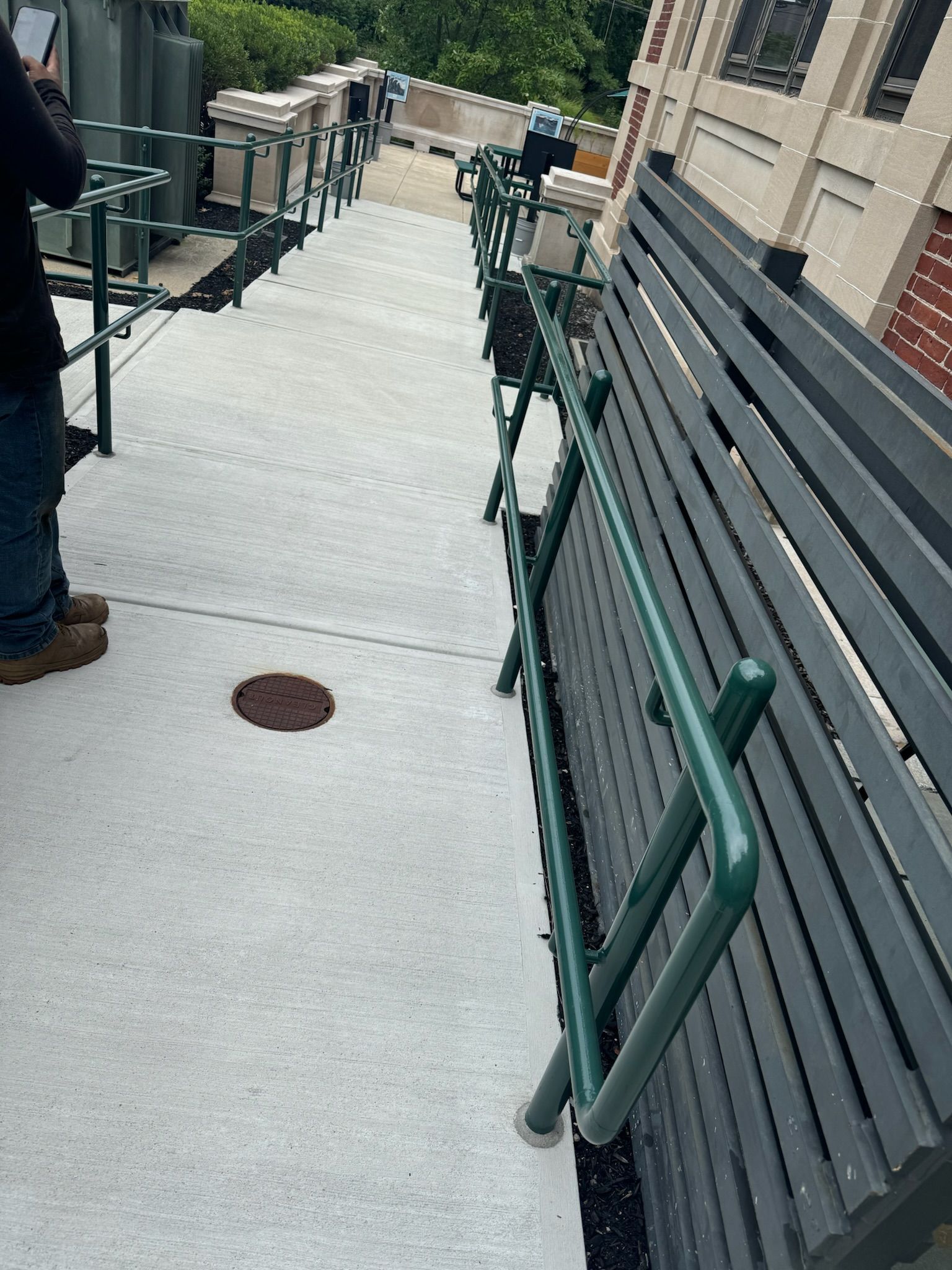 Outdoor walkway with green railings, black benches, and a person standing at left.
