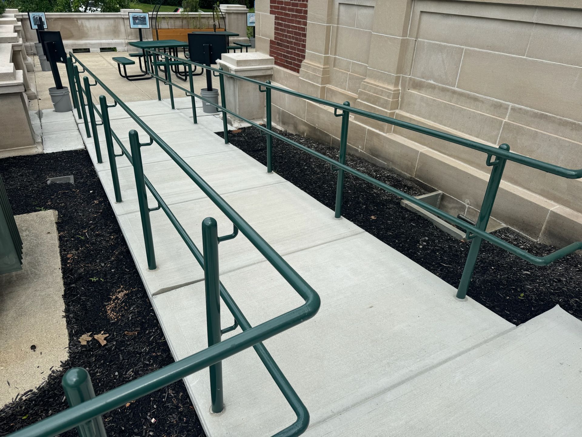 Accessible walkway with green railings and ramps leading to a building entrance