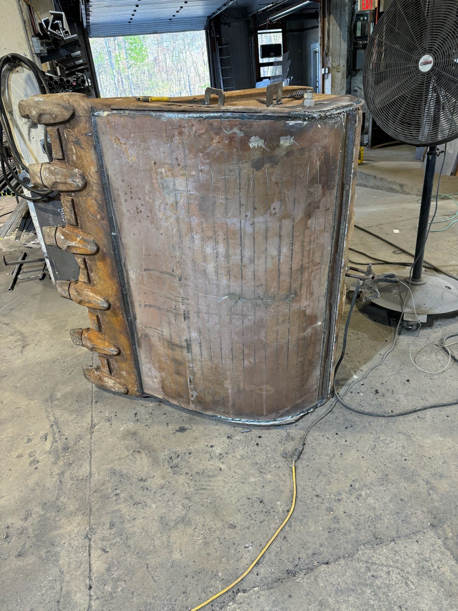 Rusty metal industrial tank in a workshop, with pipes and equipment nearby on a concrete floor.
