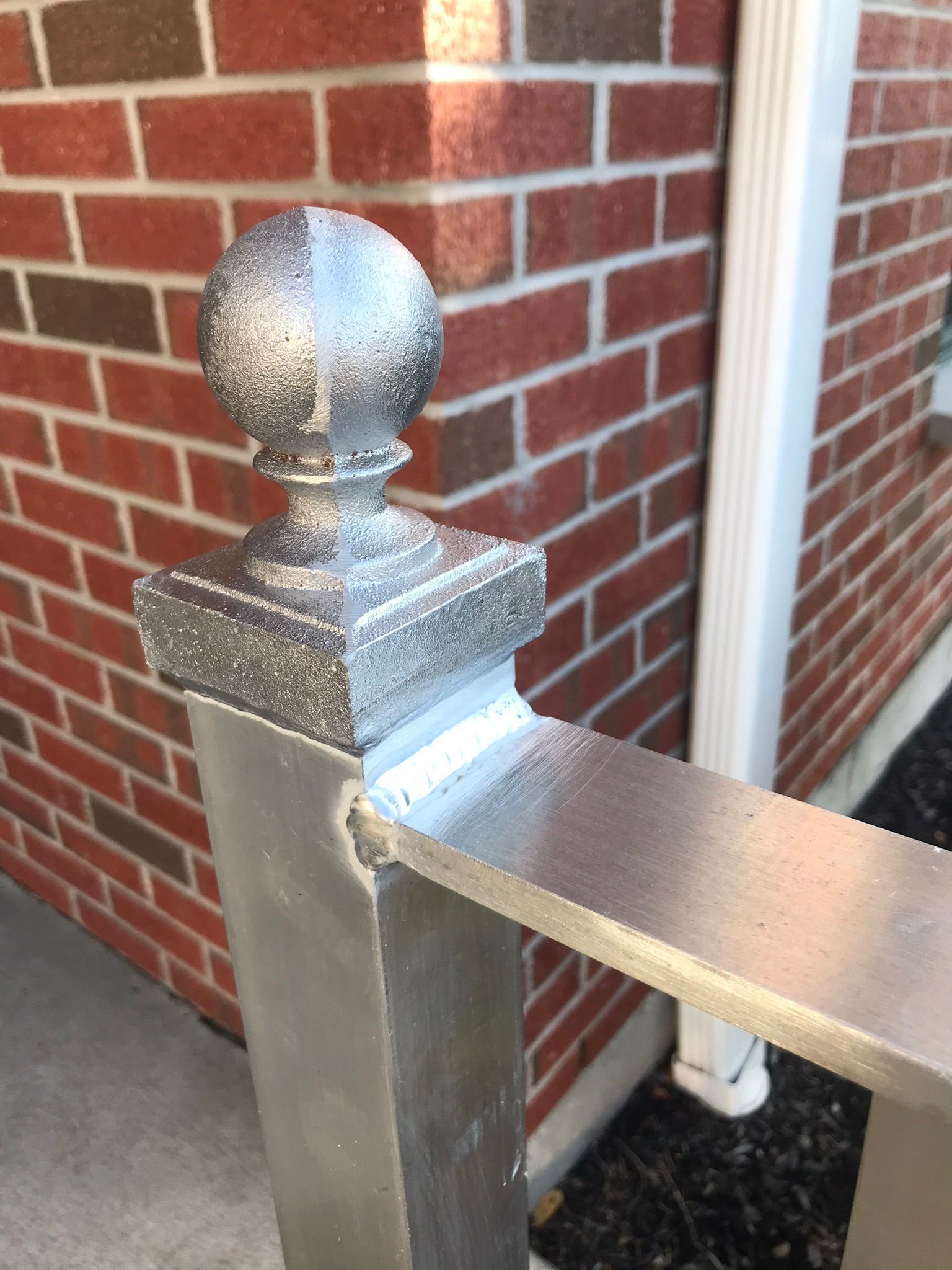 Metal post cap on a brick porch railing beside a white downspout