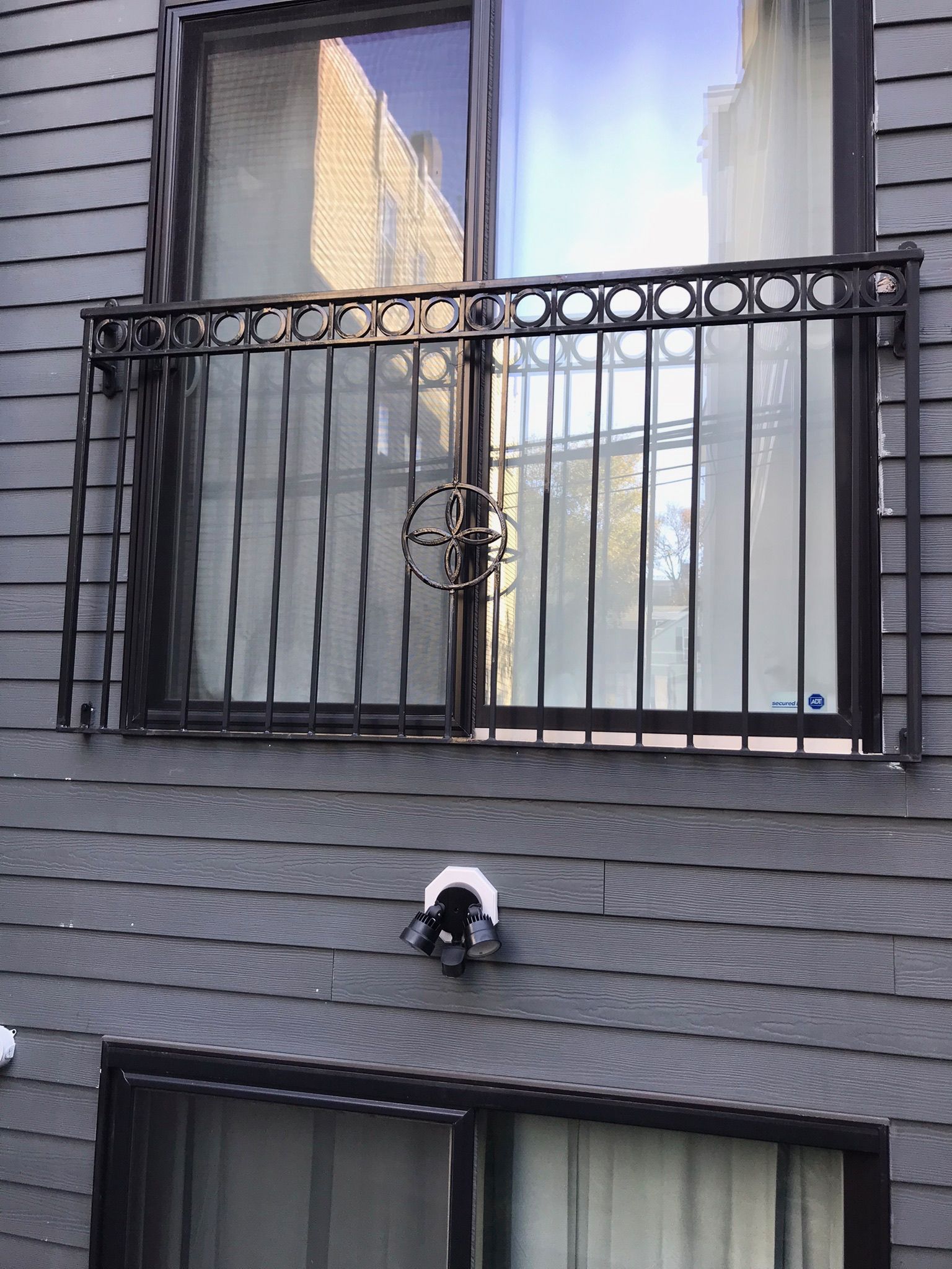 Apartment building facade with barred windows and a small black-and-white wall-mounted device between floors