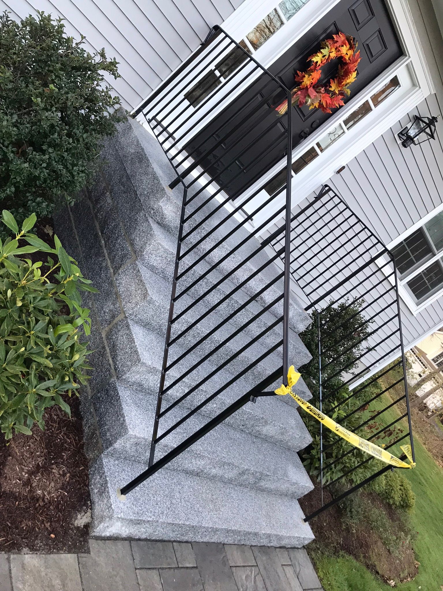 Patio deck with black railing, potted flowers, and yellow caution tape by a house exterior.