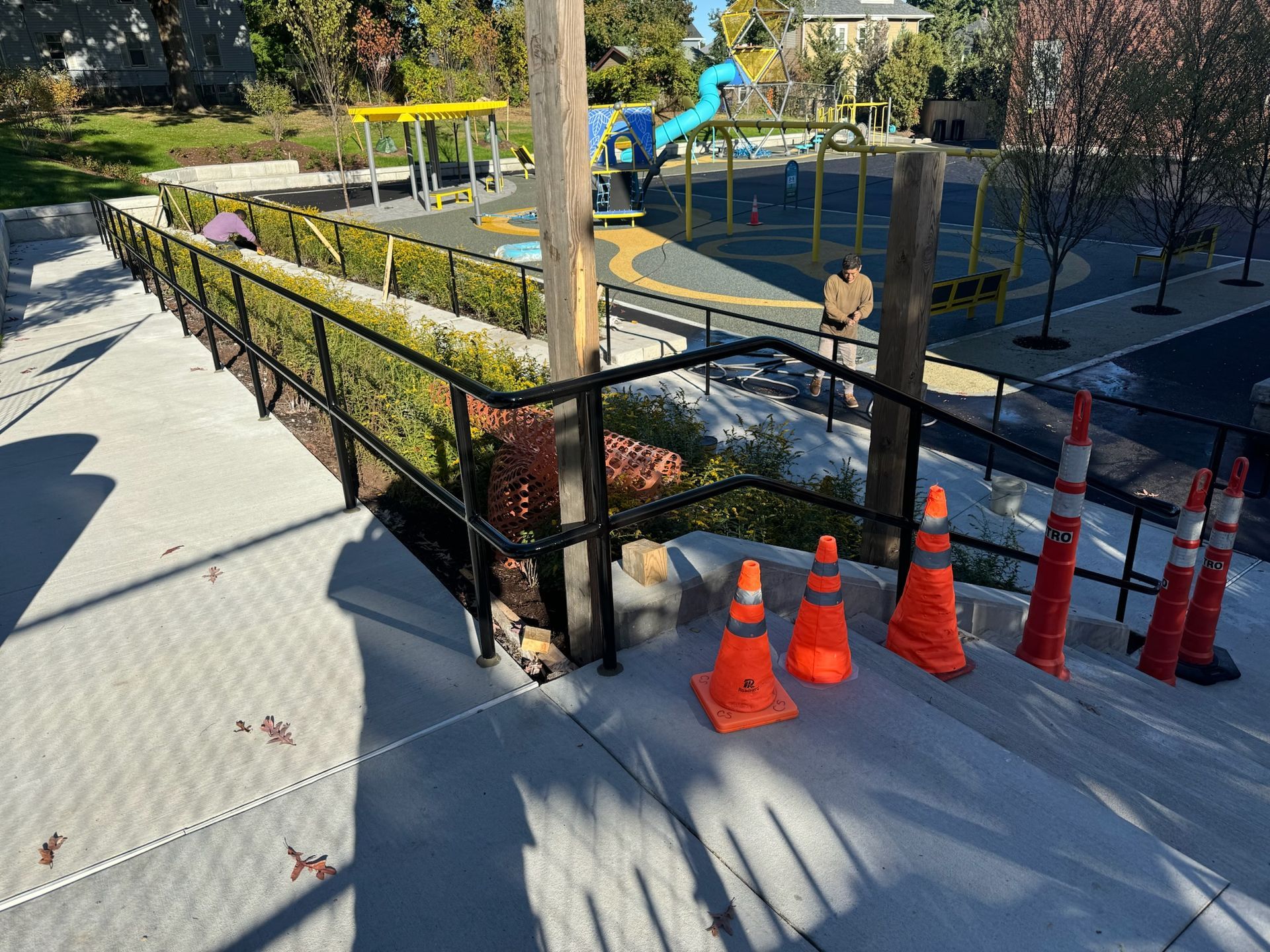 Outdoor playground ramp with black railing, orange traffic cones, and yellow play equipment in the background