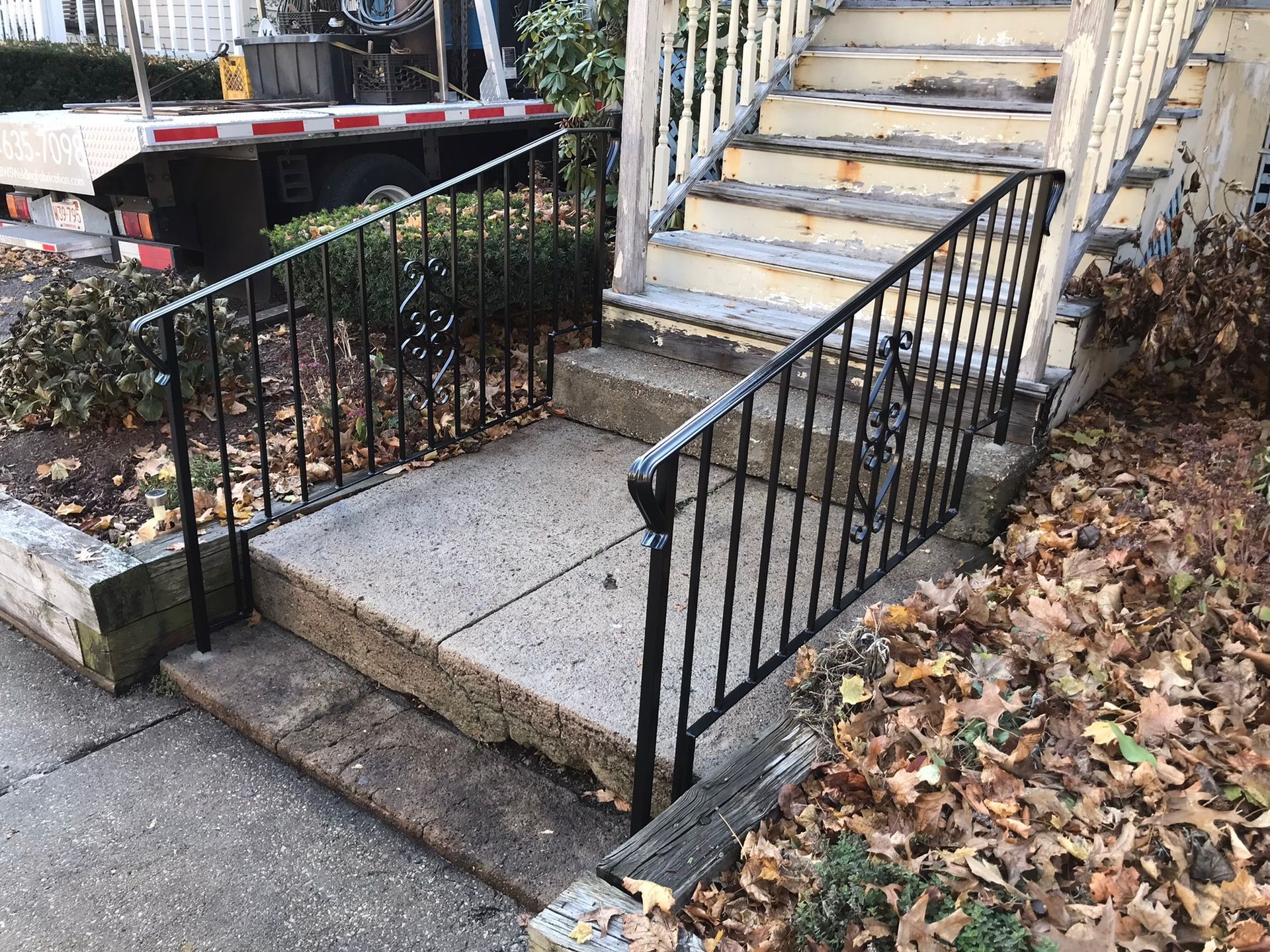 Accessible concrete ramp and stairs with black metal railings beside a leaf-covered sidewalk