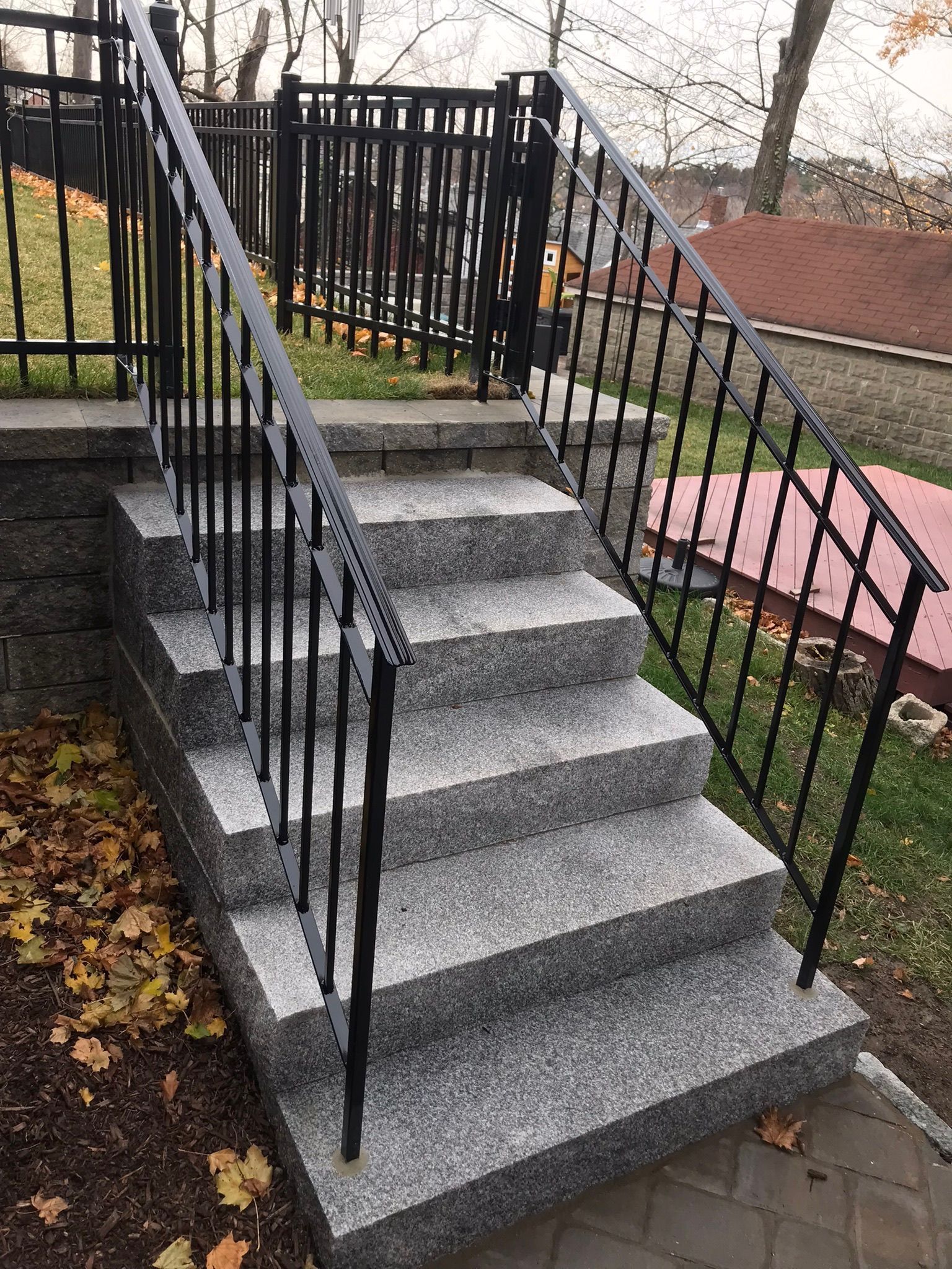 Outdoor concrete steps with black railings and a pink walkway beside them, lined with fallen leaves.