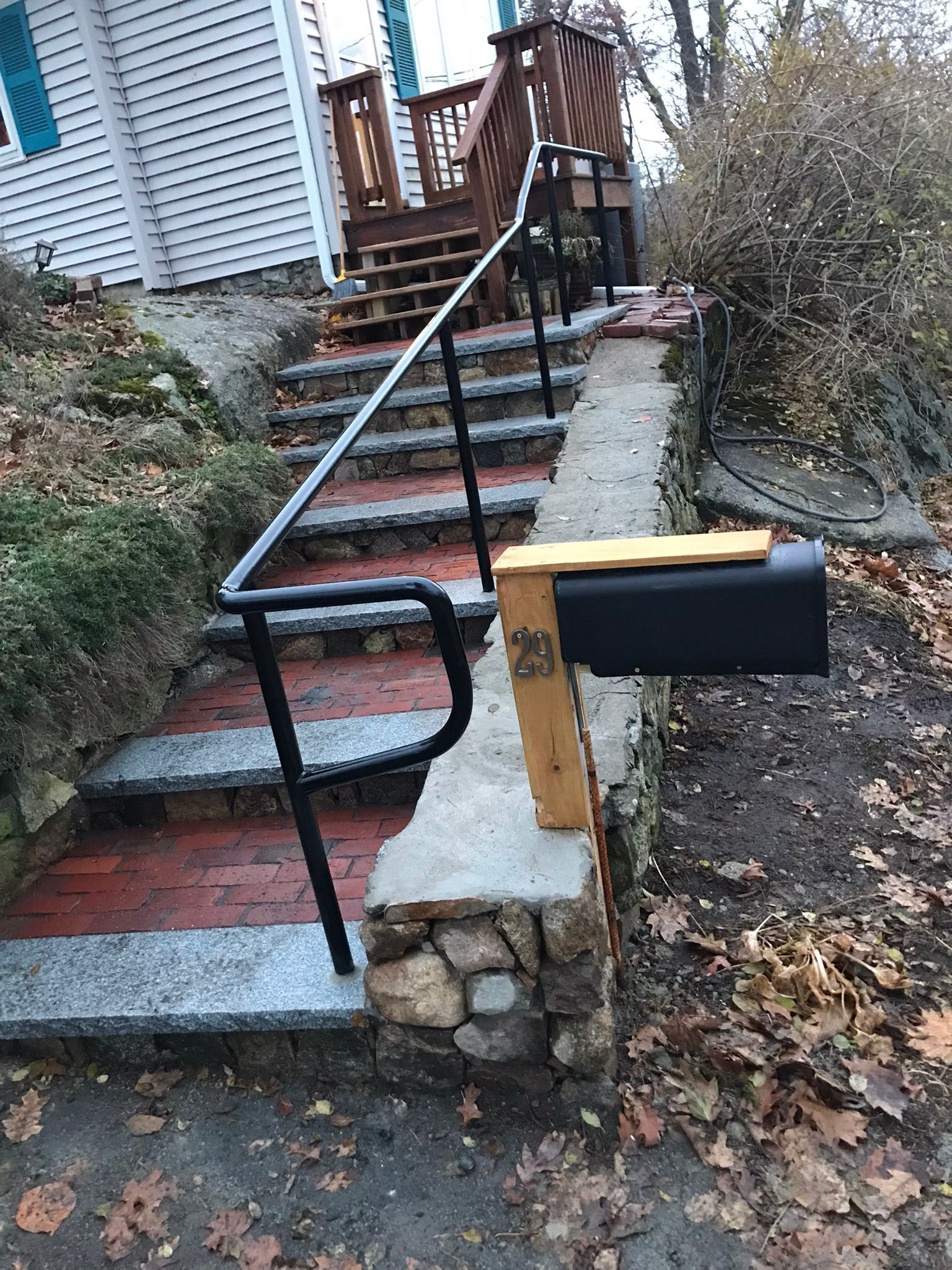 Steep outdoor stairs with black handrail and narrow brick ramp beside a house, next to a mailbox.