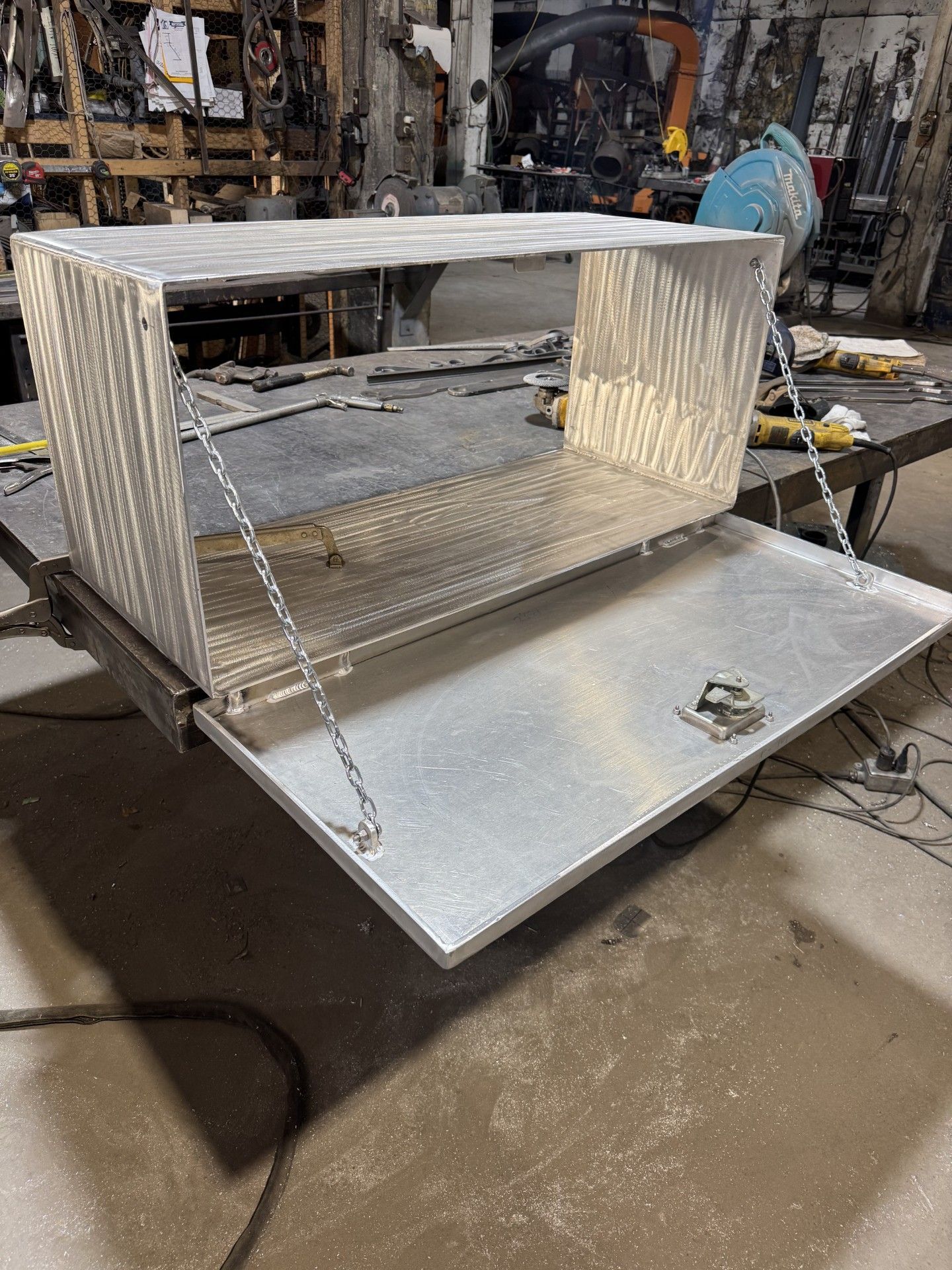 A metal industrial enclosure with an open front sits in a workshop, showing a shiny slanted base.