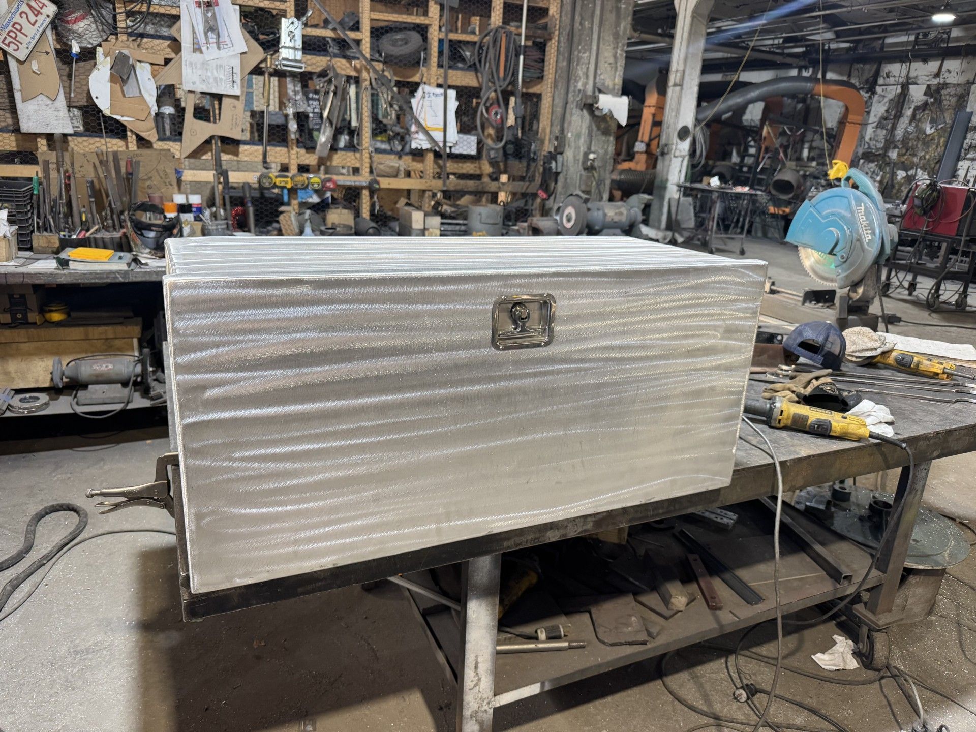 Large silver metal chest on a workshop table, with tools and cluttered equipment in the background.