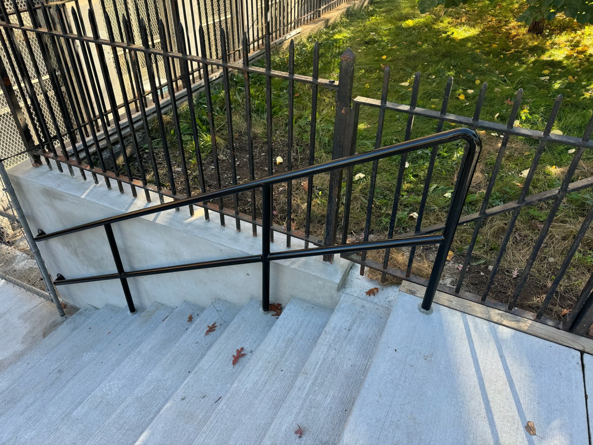 Concrete outdoor stairs with black metal railings beside a fence and grassy area