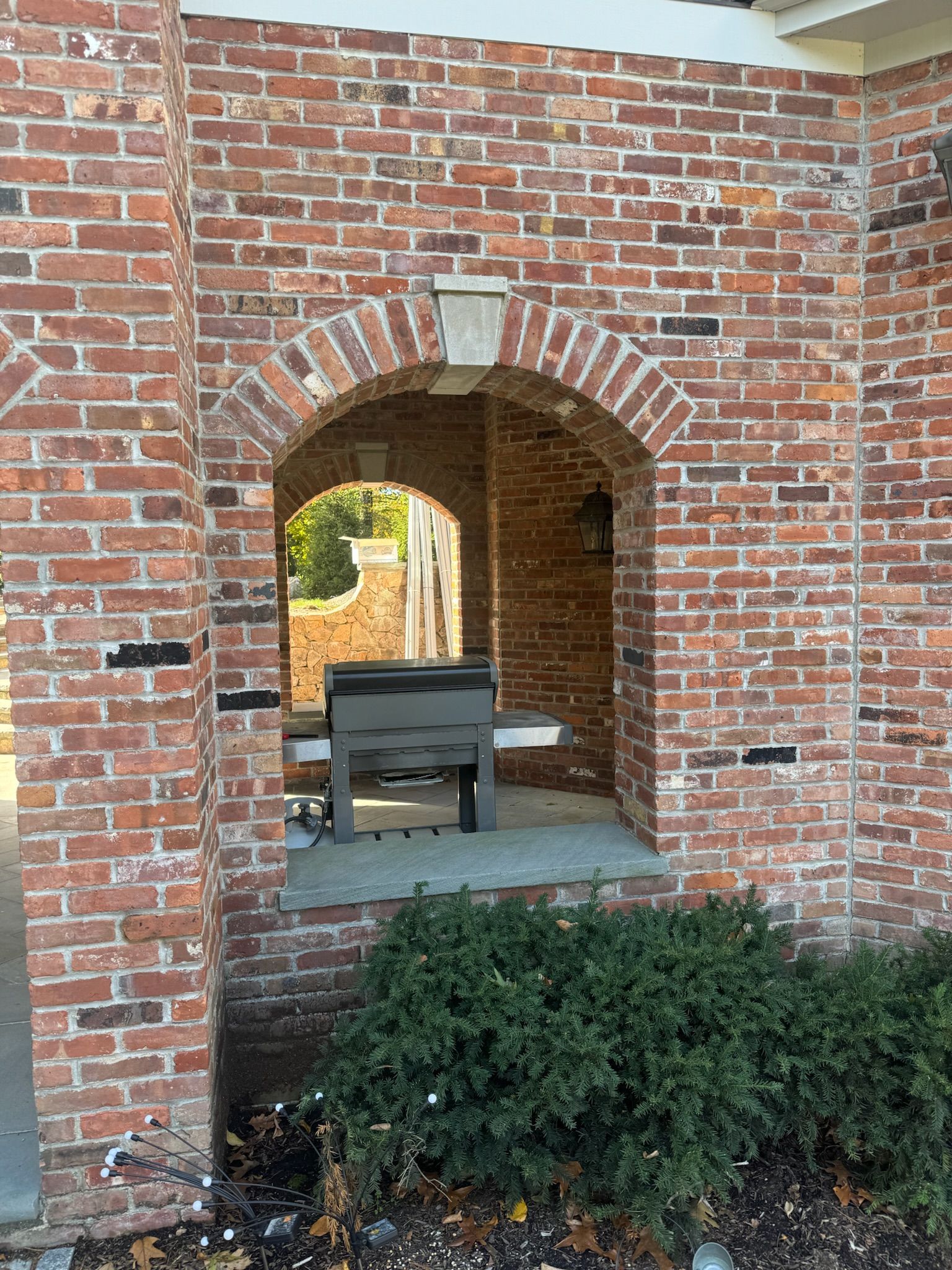 Brick archway with a stone bench and greenery in front of a brick wall
