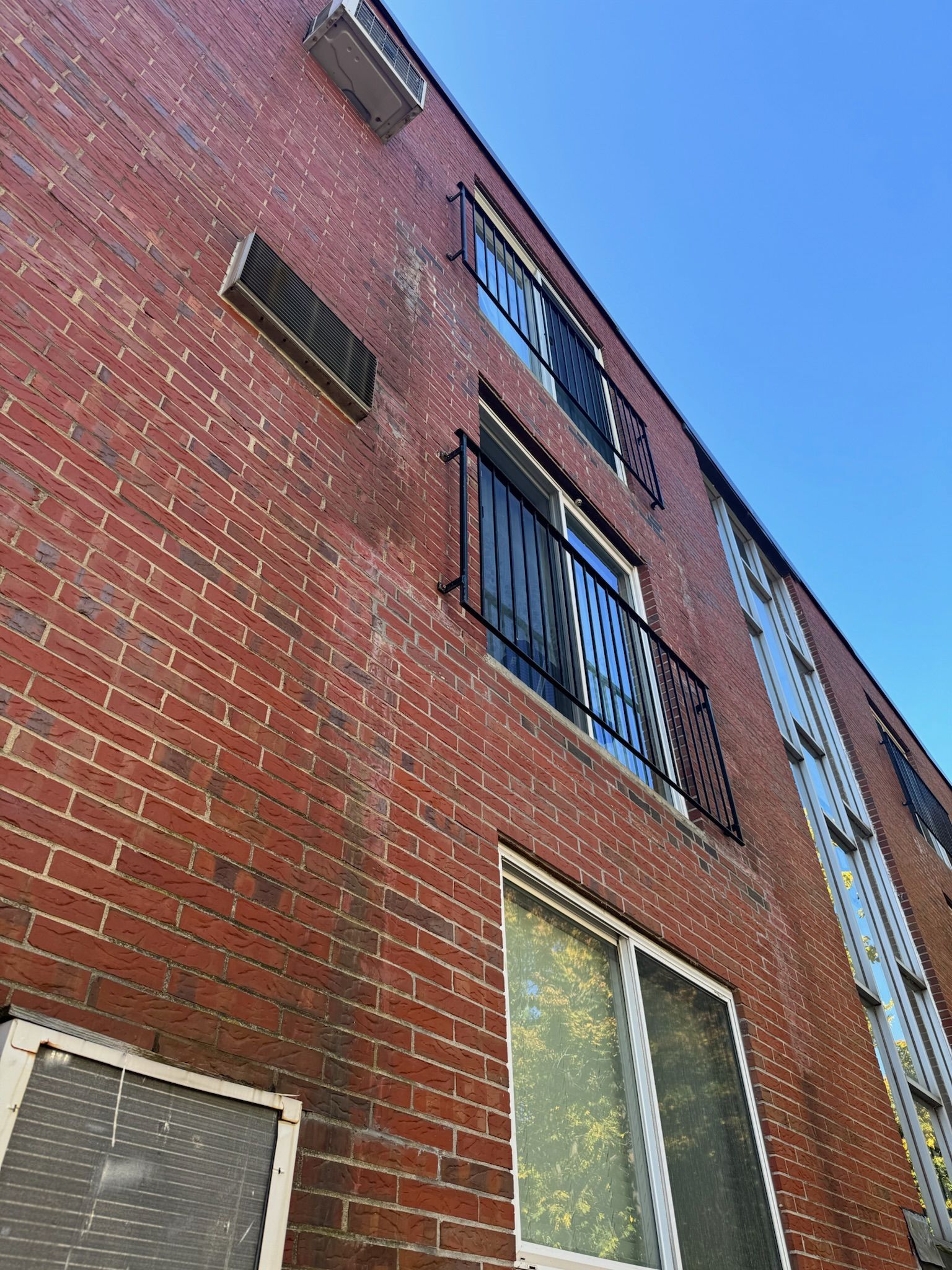 Brick apartment building facade with barred windows viewed from below against a blue sky