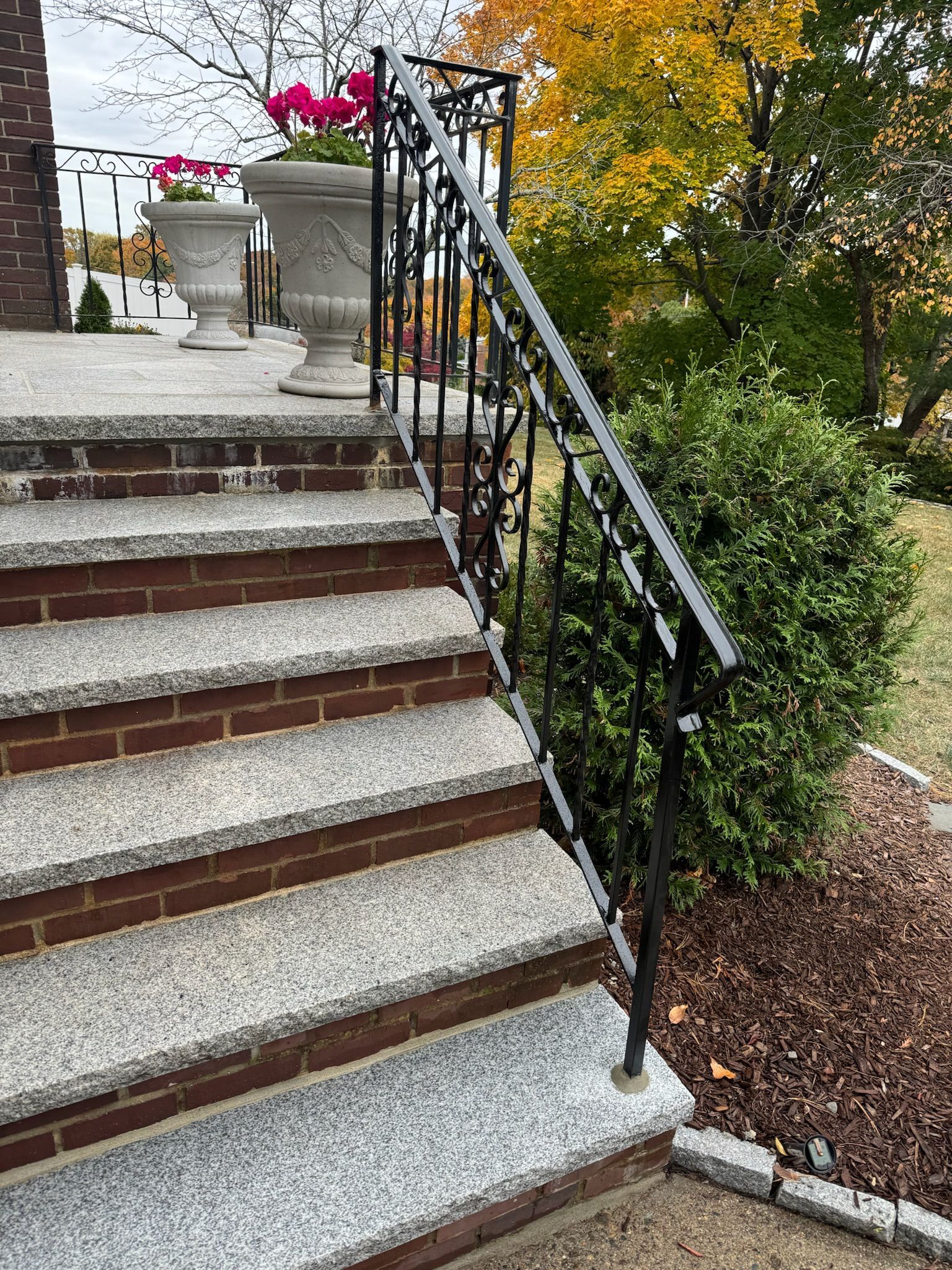 Stone steps with black wrought-iron railing beside autumn shrubs and flowers