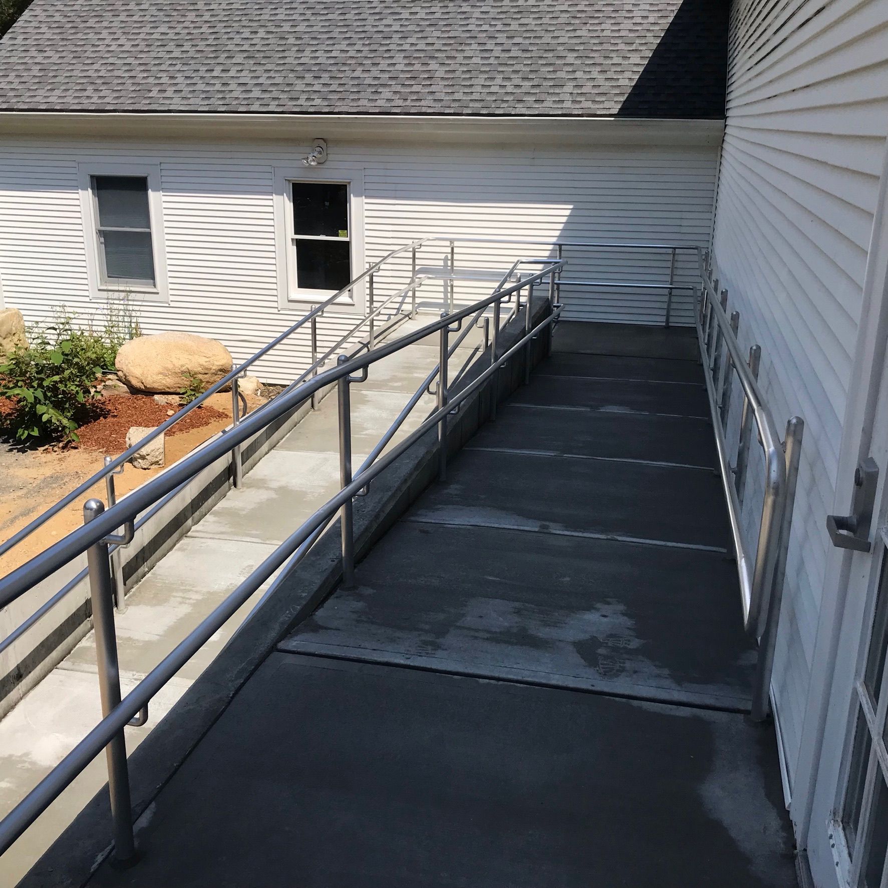 Exterior wheelchair ramp beside a white building, with black railings and concrete walkway.