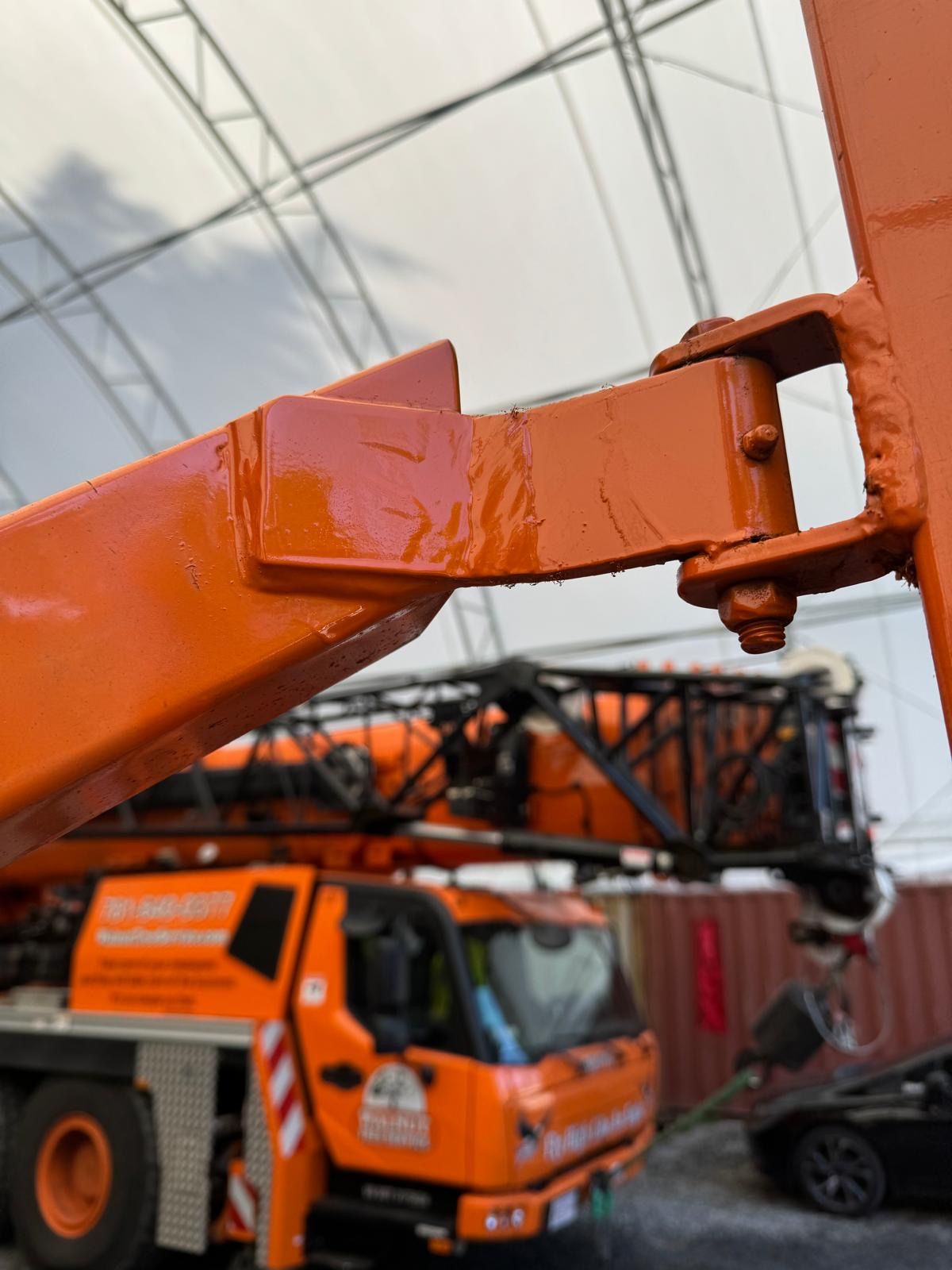 Orange boom lift arm close-up with a construction truck and covered worksite in the background