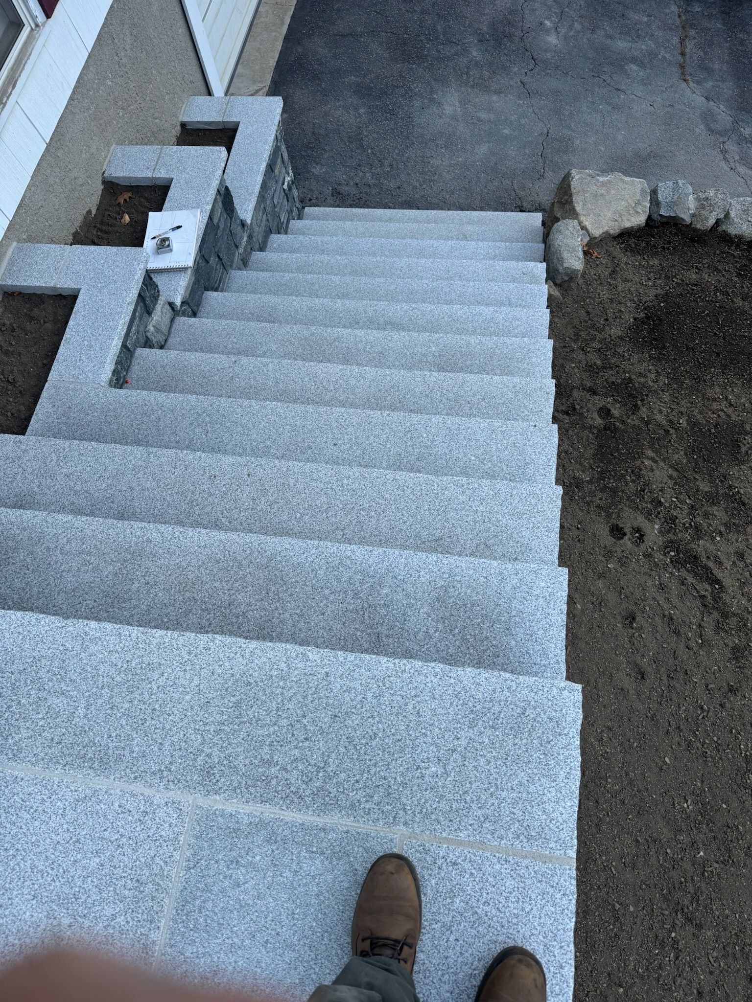 Concrete outdoor stairs viewed from above, with a foot on the bottom step and a low wall on the left.