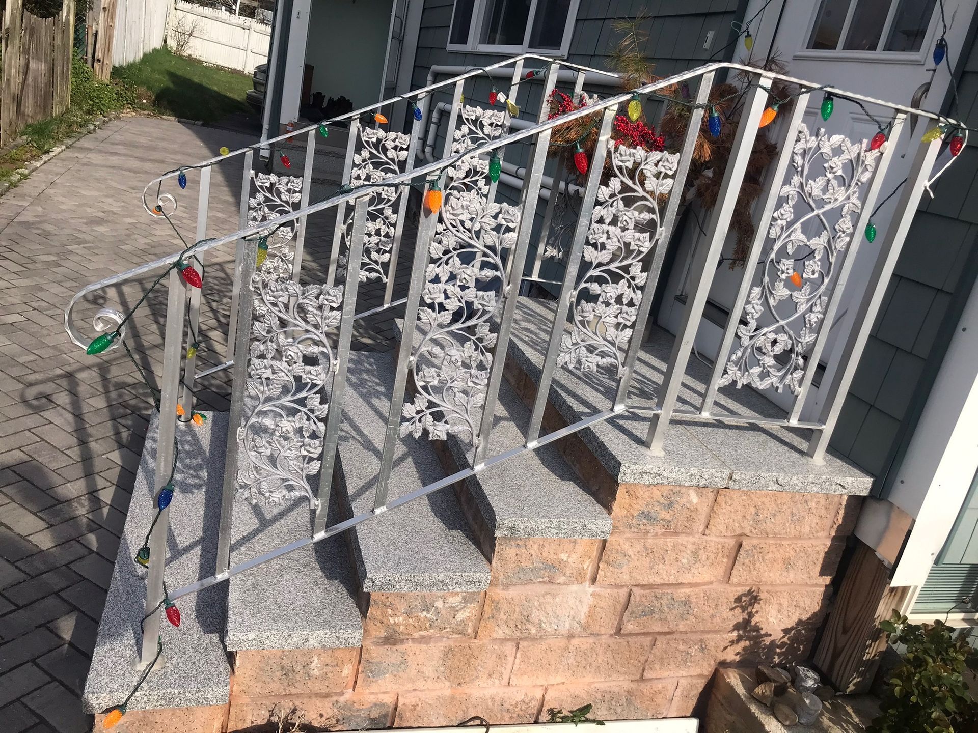 Outdoor stone steps with a white metal handrail decorated with colorful holiday lights and ornaments
