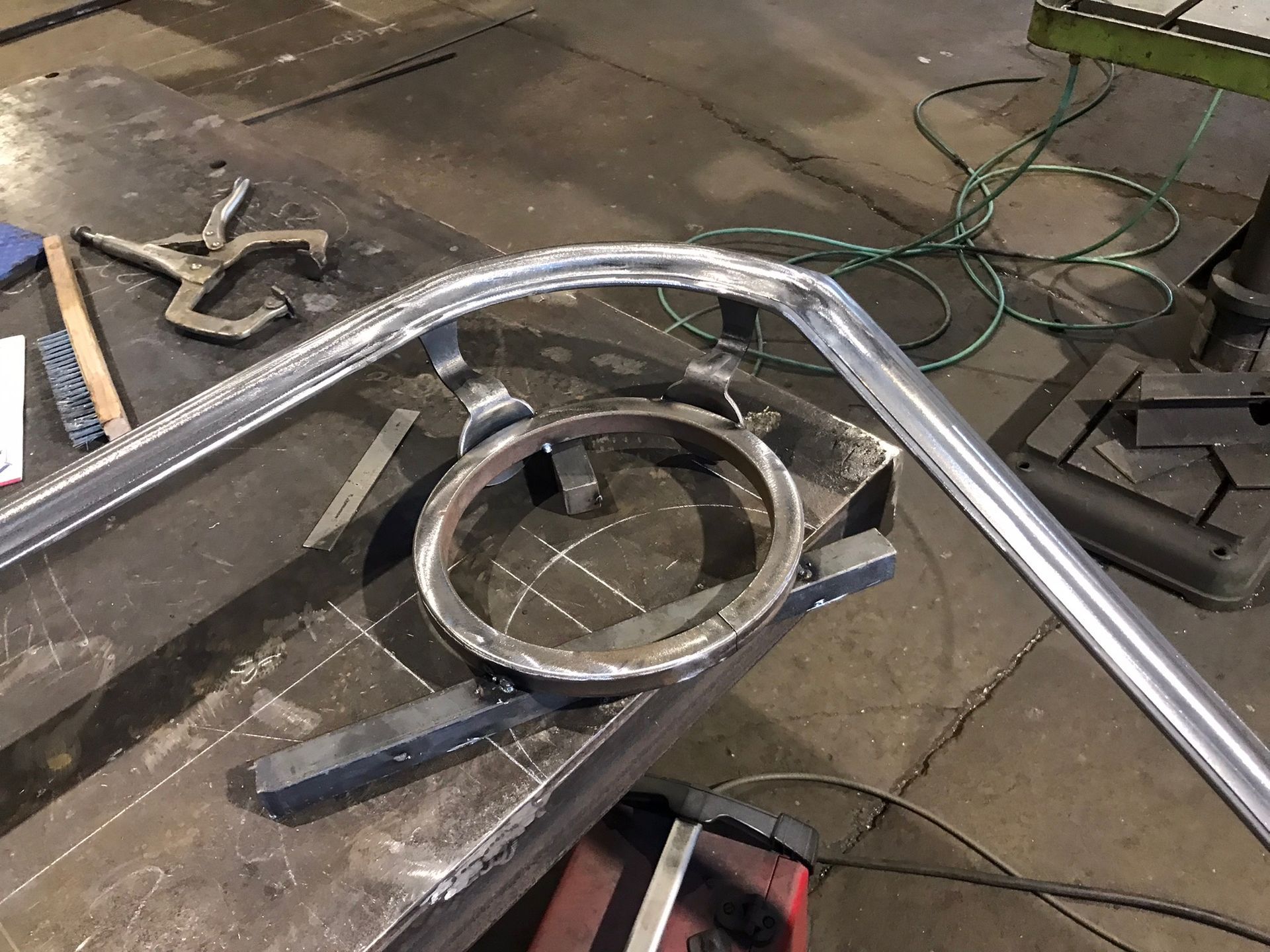 Bent chrome metal tubing bent into a frame on a workshop floor, with tools and scrap nearby