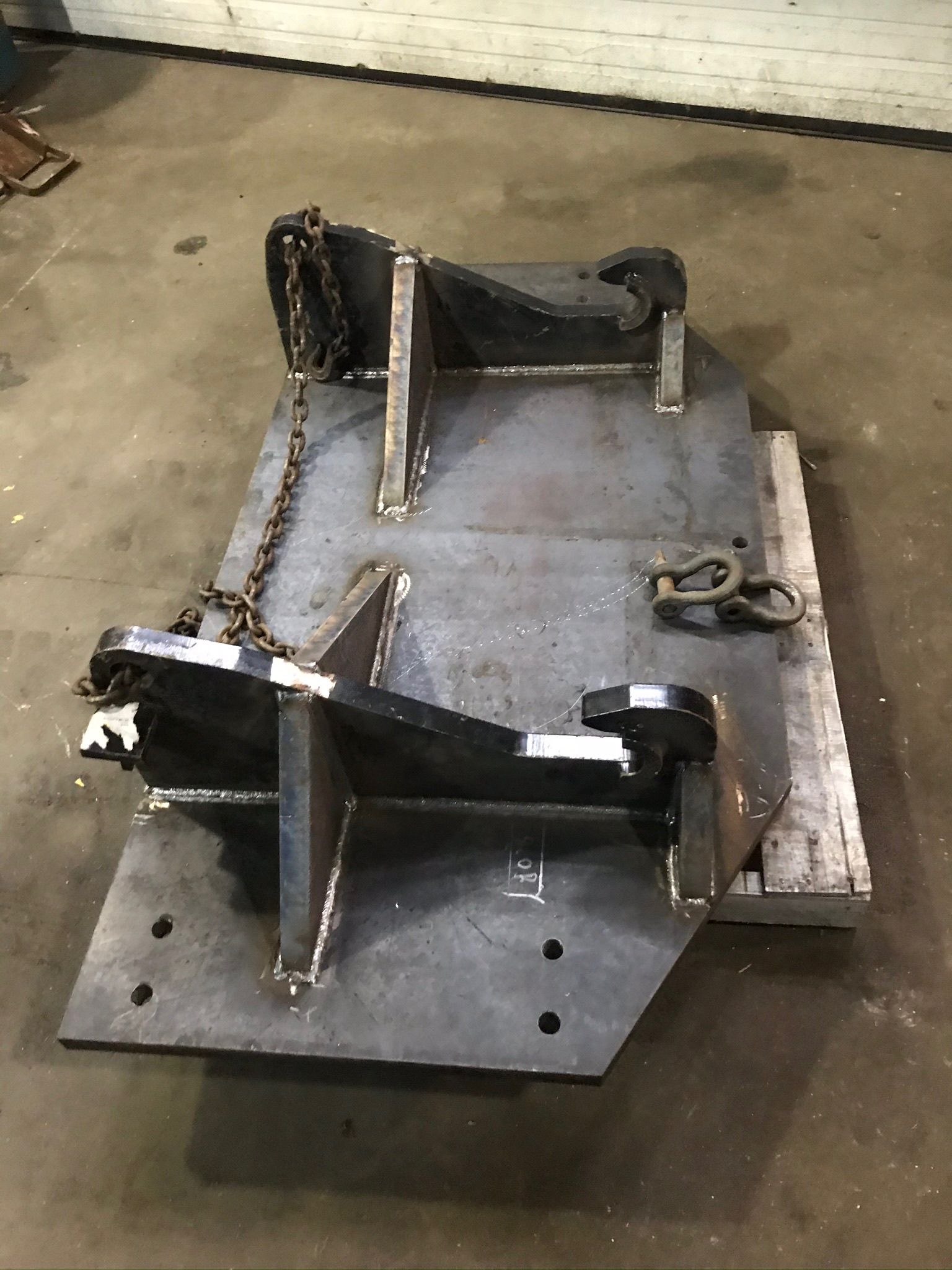 Metal fabrication jig with black steel brackets and clamps mounted on a wooden base in a workshop.