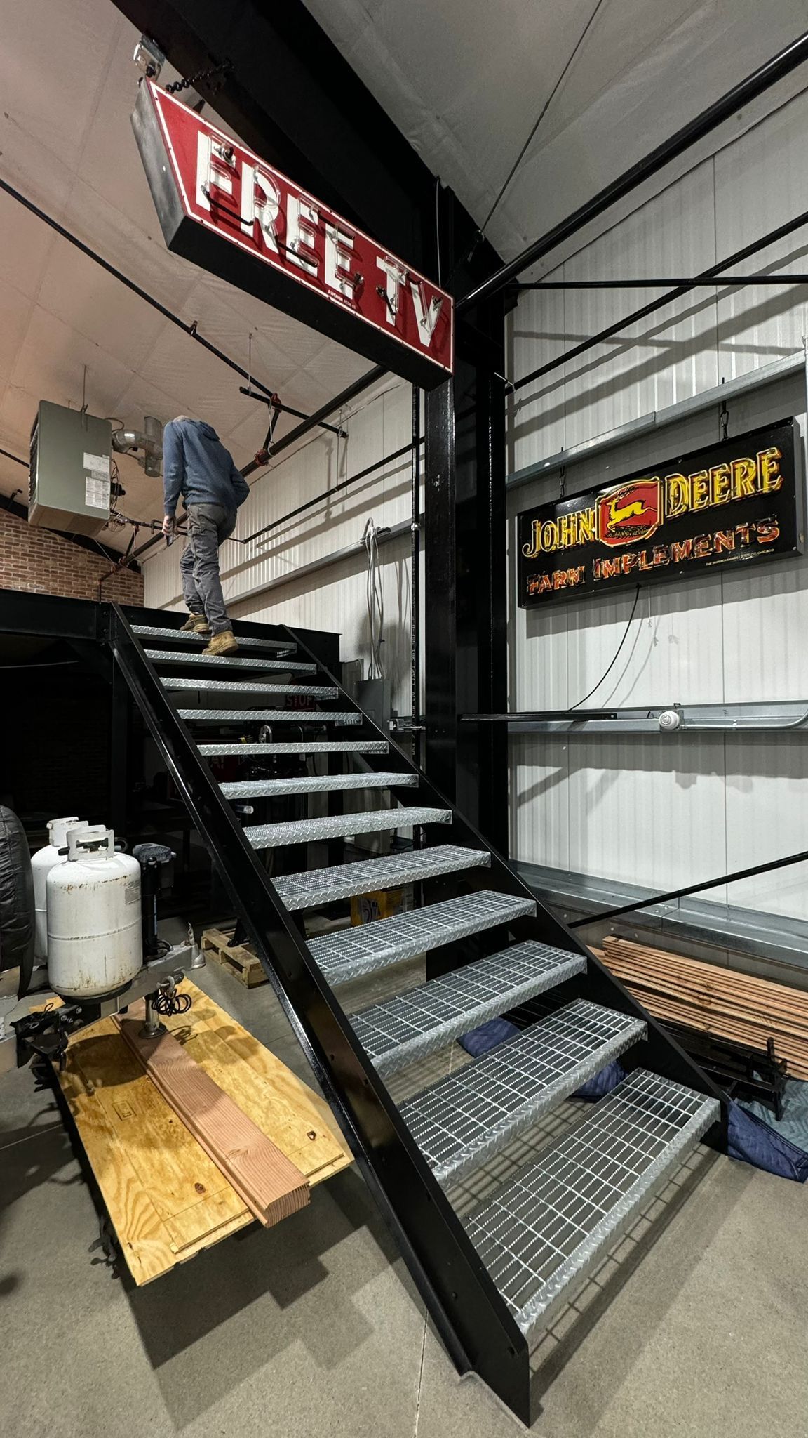 Metal staircase inside warehouse with a worker installing a red sign overhead